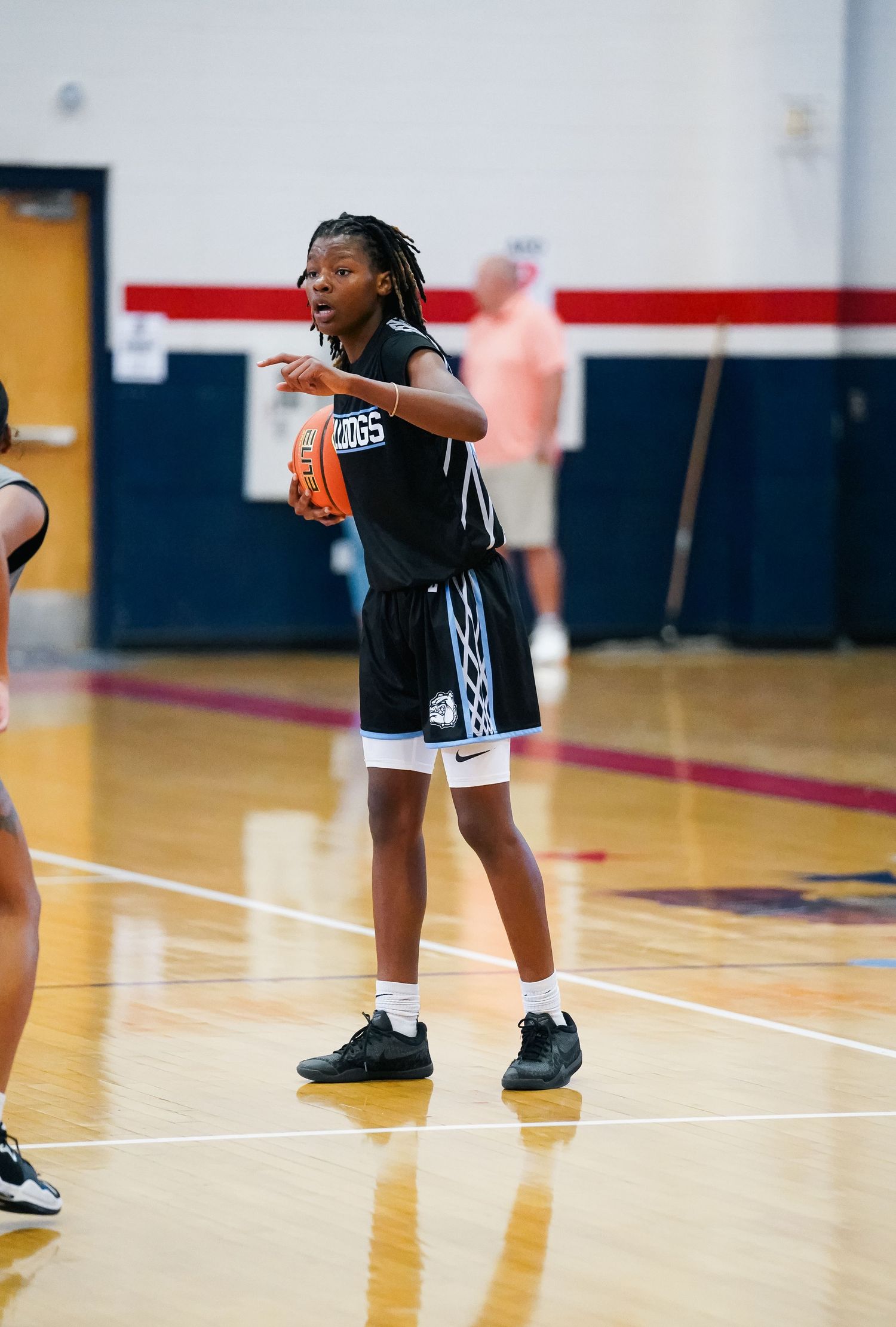Youth basketball player in black jersey practices defensive moves on wooden court.