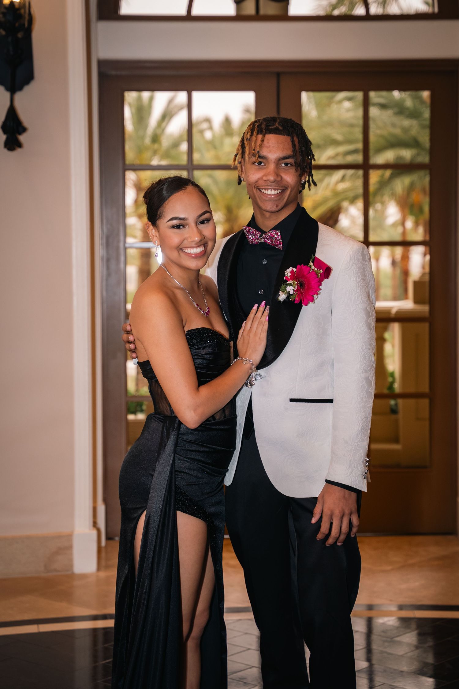 Couple in formal black and white attire pose in elegant venue with warm lighting.