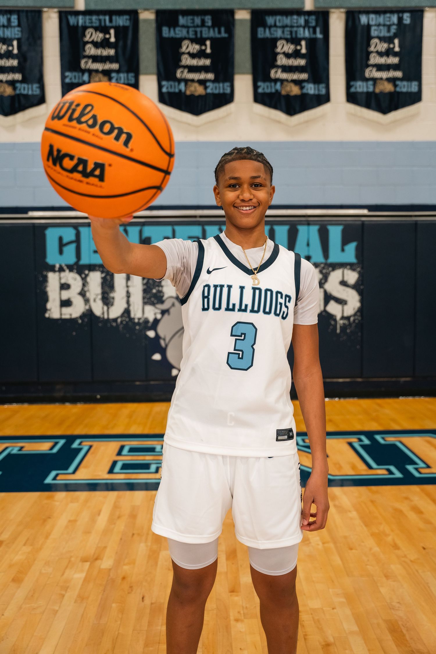 Basketball player in white Bulldogs uniform number 3 holds up Wilson NCAA basketball with championship banners.