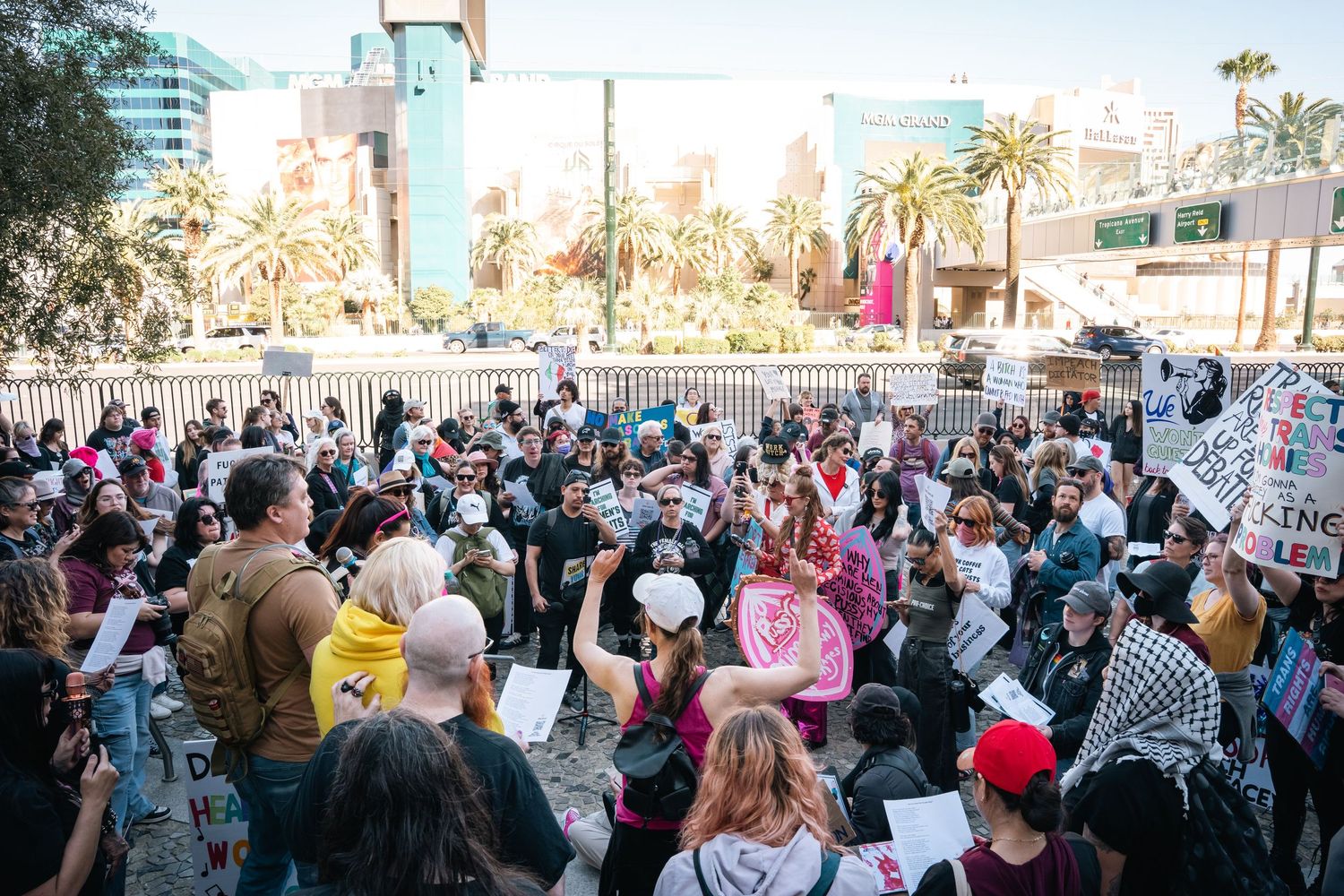 Large crowd of protesters gathering in an outdoor urban area with signs.