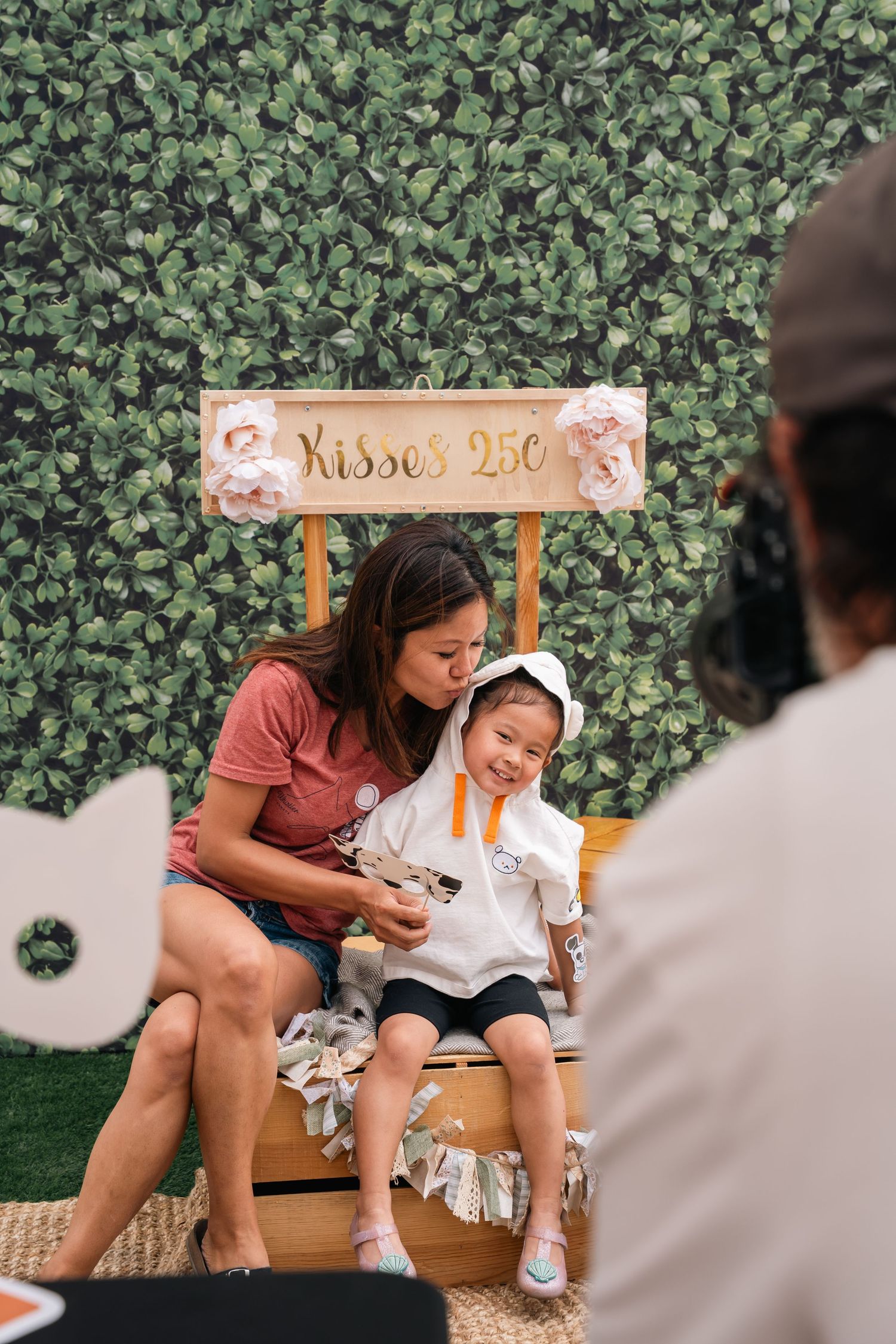 Photo booth scene with greenery wall backdrop and wooden 'Kisses' sign.