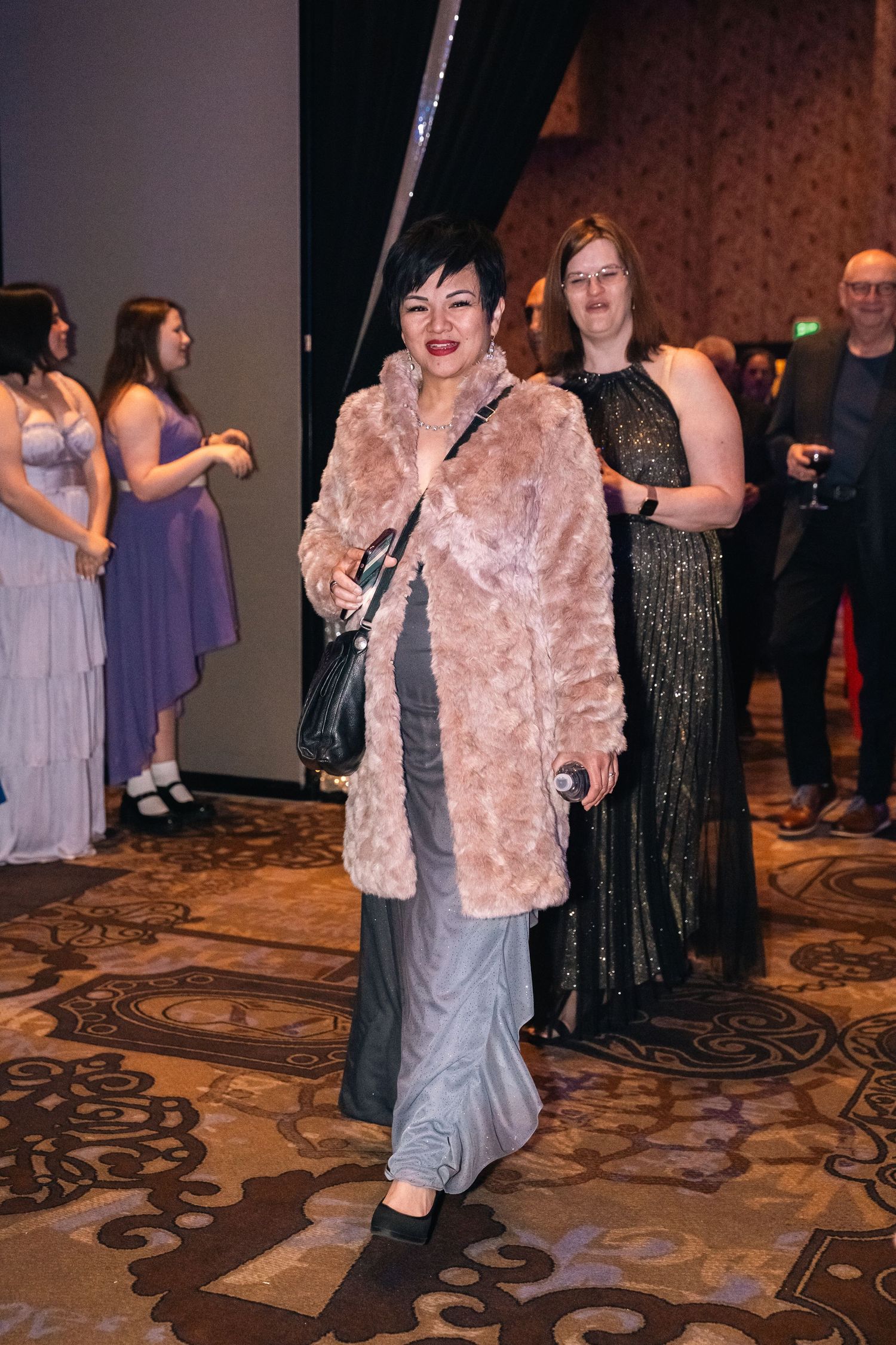 Event attendee wearing a plush pink coat and grey dress at an elegant gala.