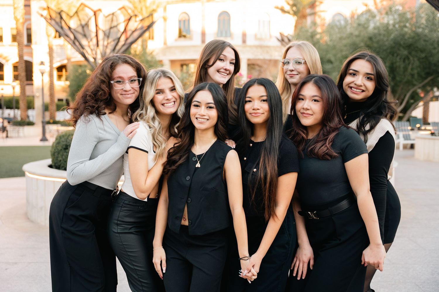 Group of friends in black and white outfits pose together in front of architectural backdrop.