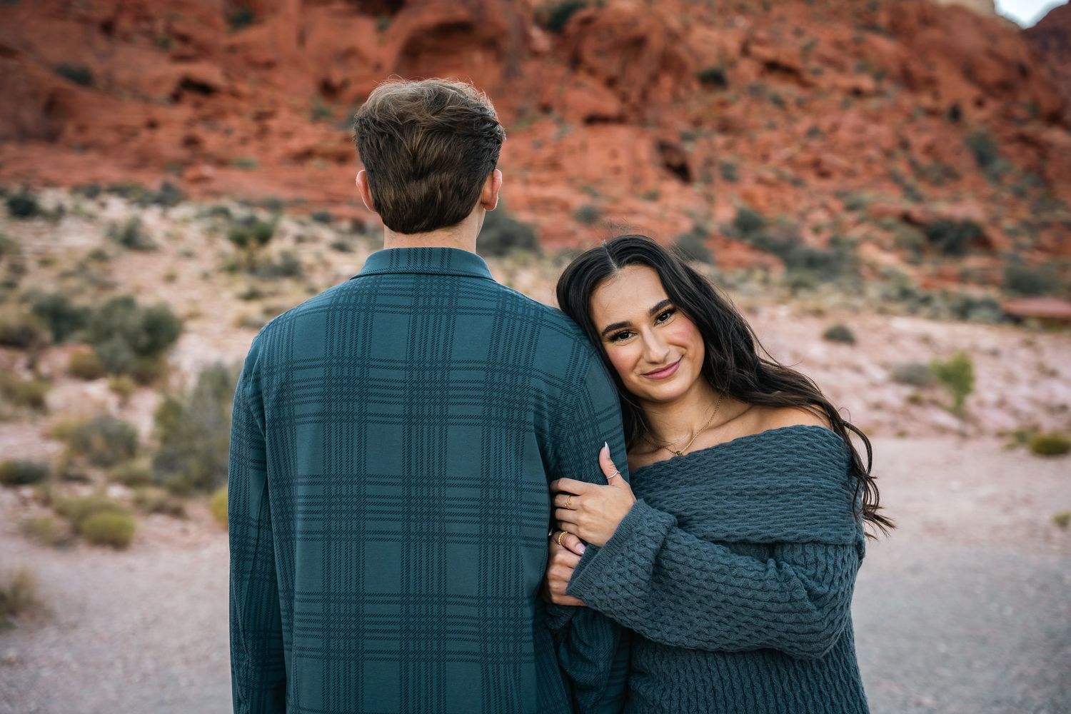 Couple in matching sweaters pose against red rock formations.