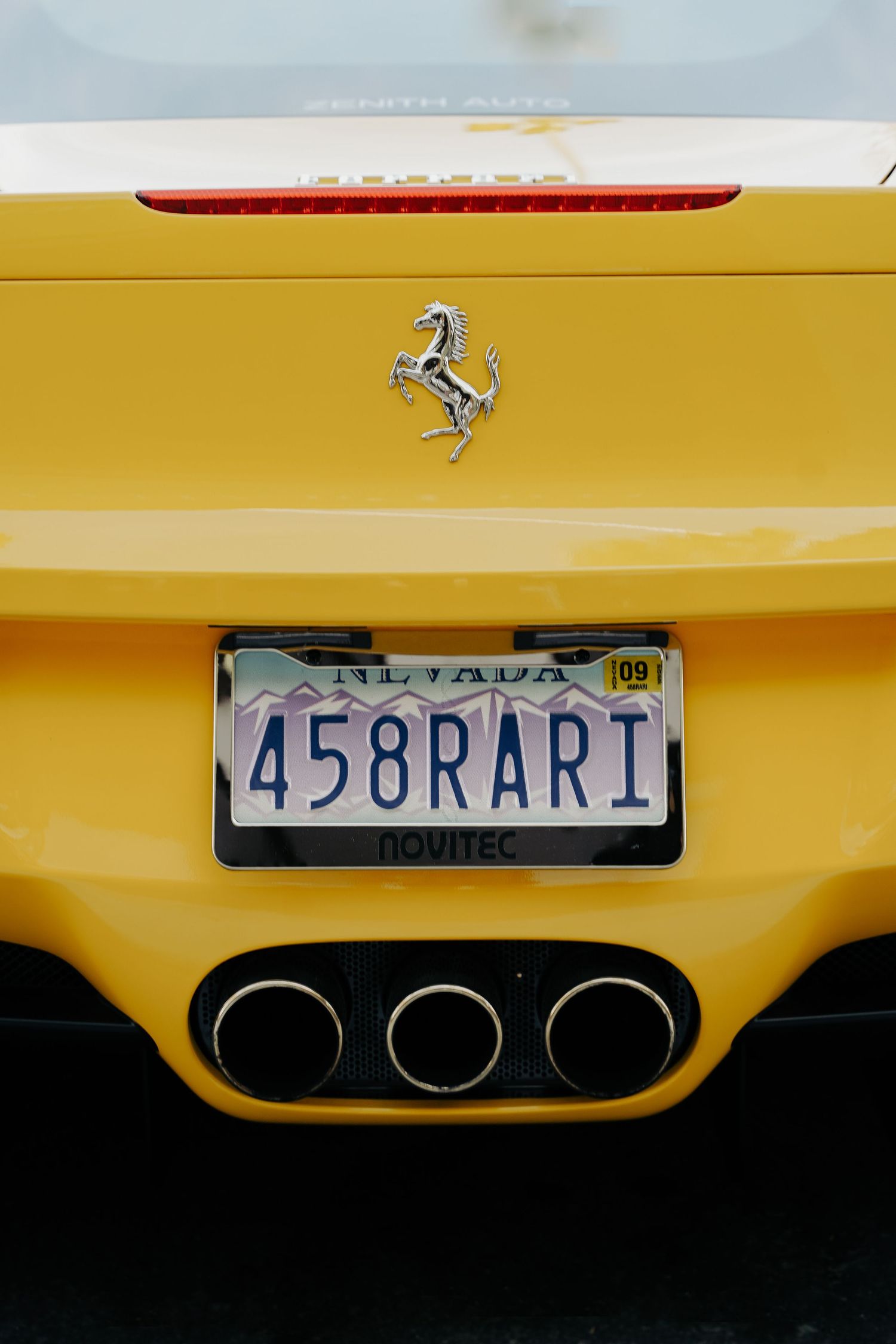 Close-up of a yellow Ferrari's rear license plate and exhaust details.