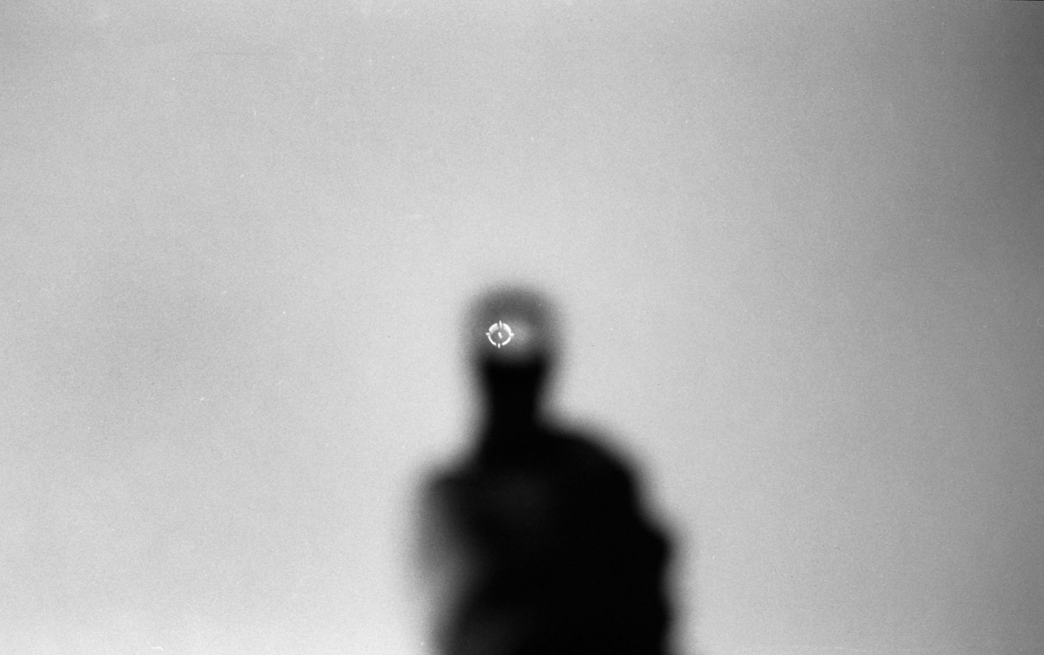 Blurred silhouette figure with glowing circular light above head against gray background.