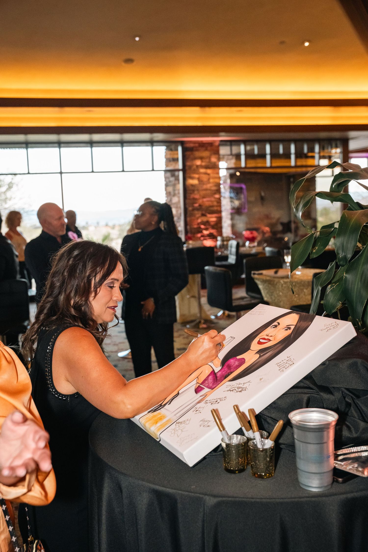 Guest signing a large portrait at an event with amber lighting and exposed brick walls.