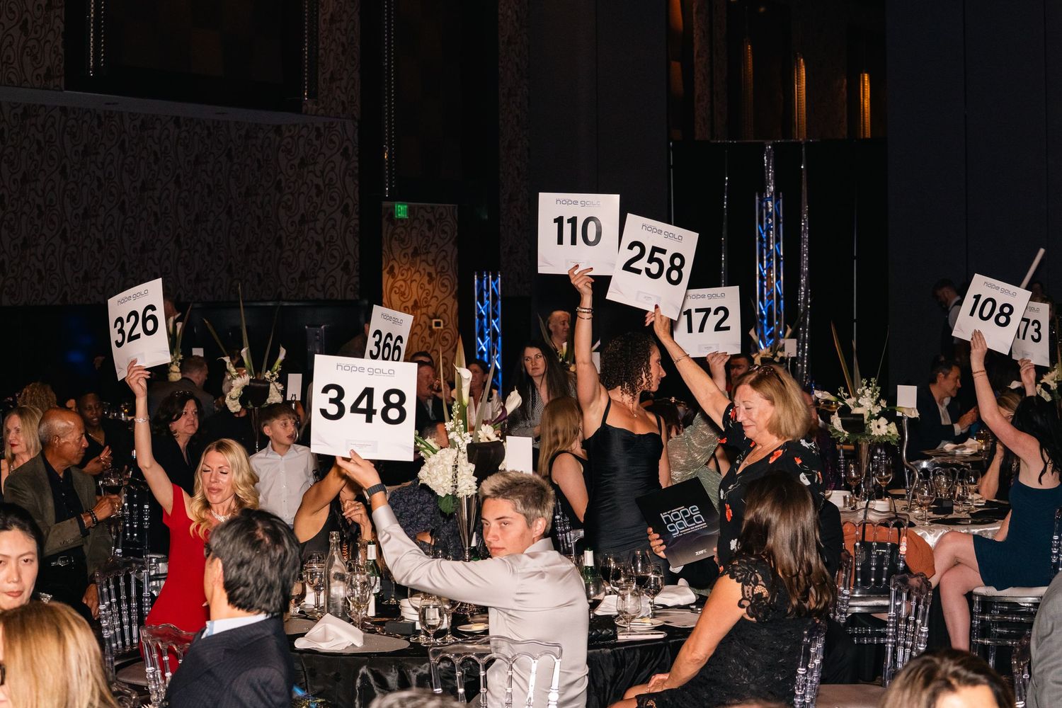 Crowd enthusiastically holding up numbered auction paddles during fundraising event.
