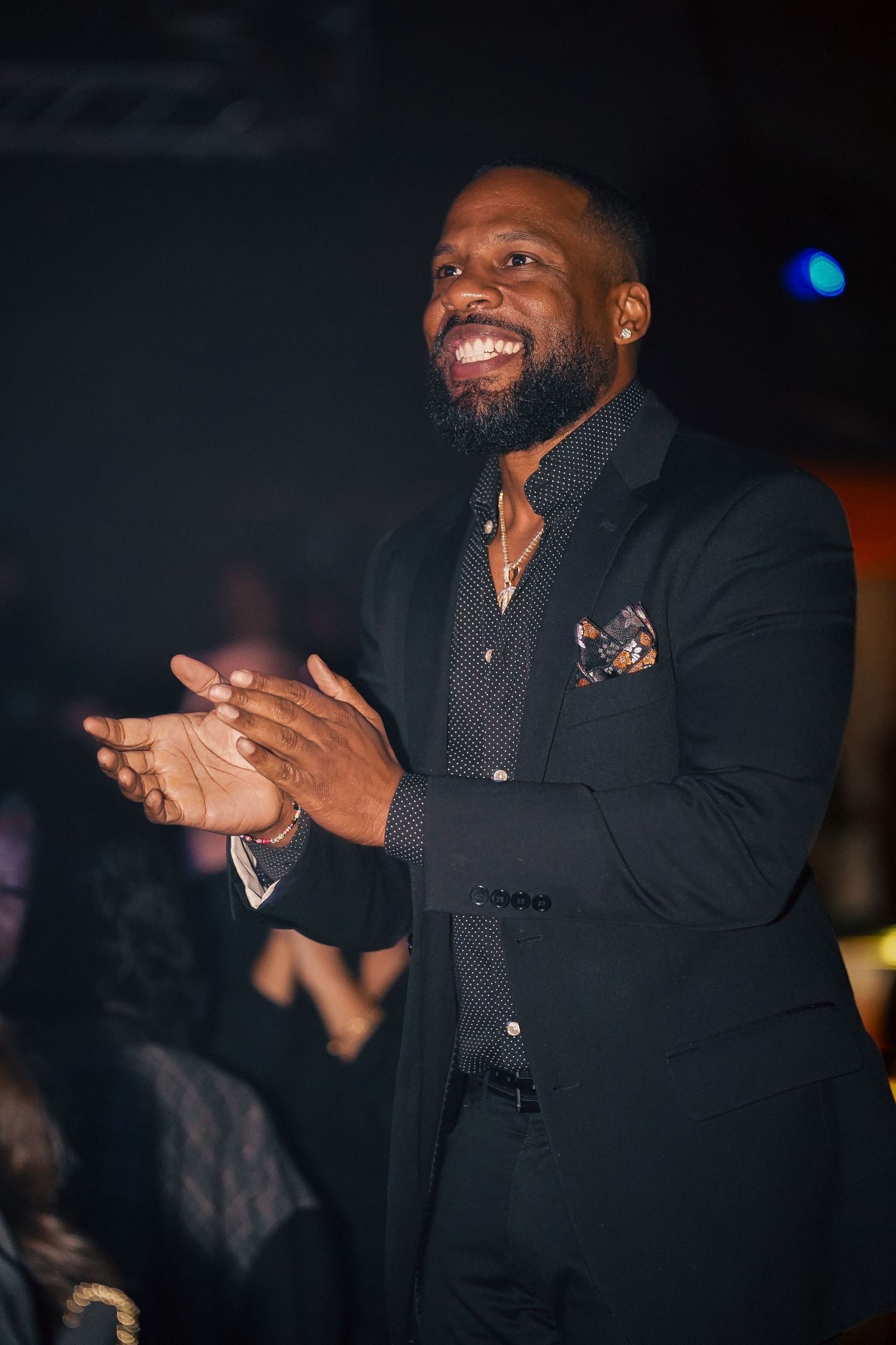 Performer in dark attire gesturing enthusiastically on stage during a nighttime show.