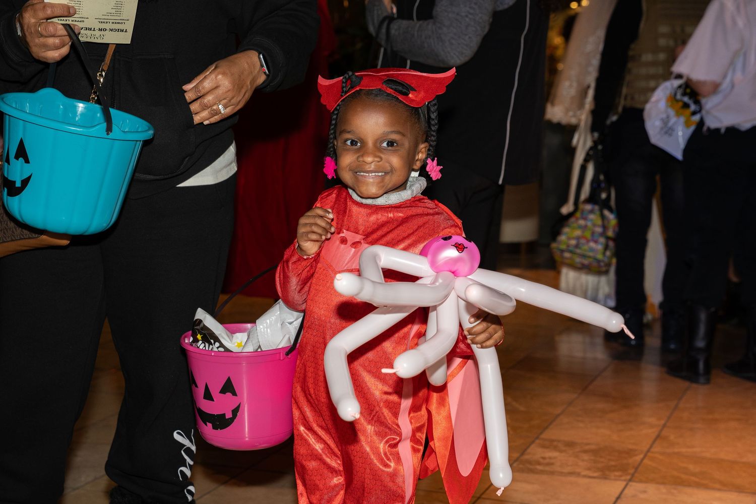 A child in a red costume holds a trick-or-treat bucket at a Halloween event.