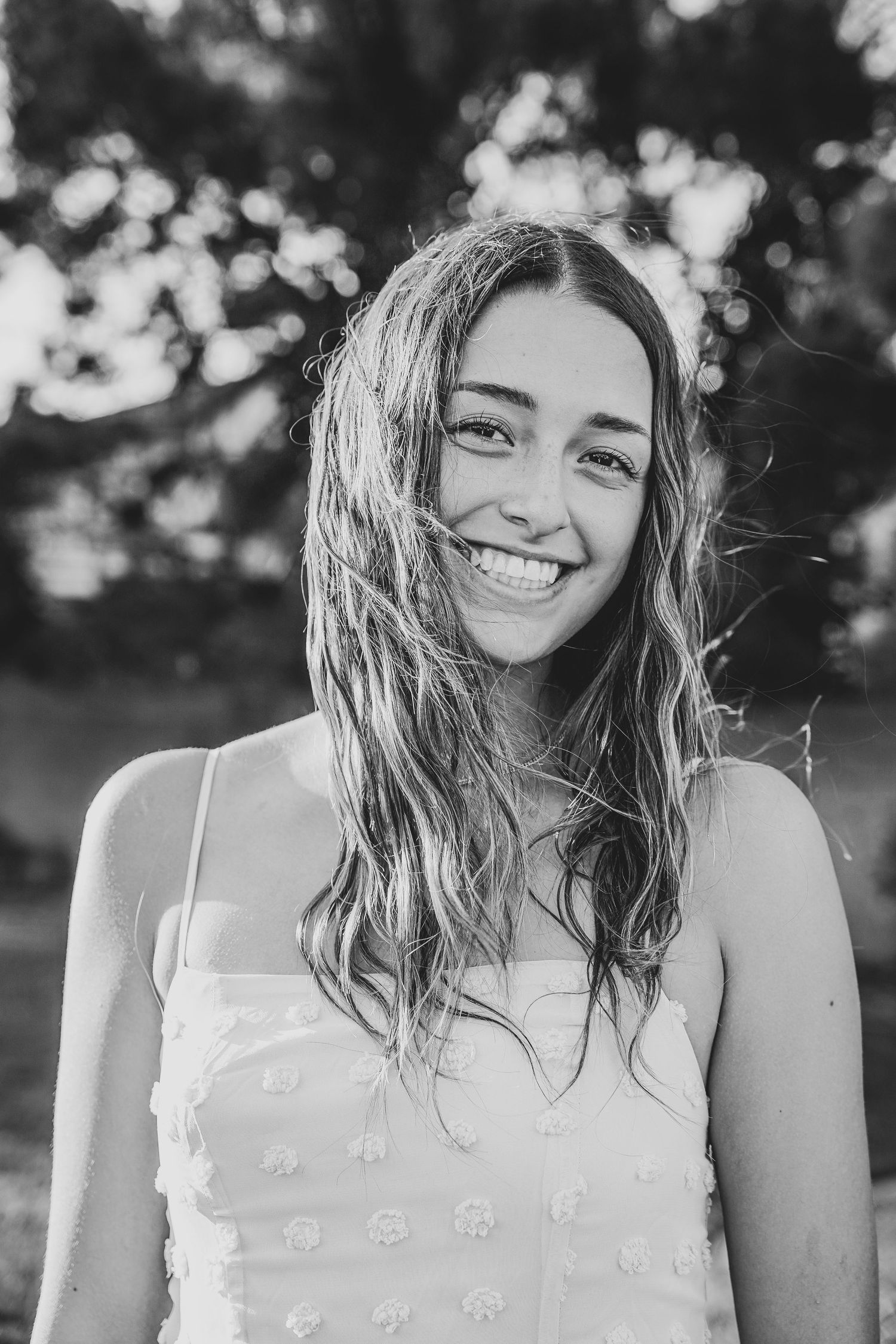 Black and white portrait of person in white dress with flowing hair outdoors.