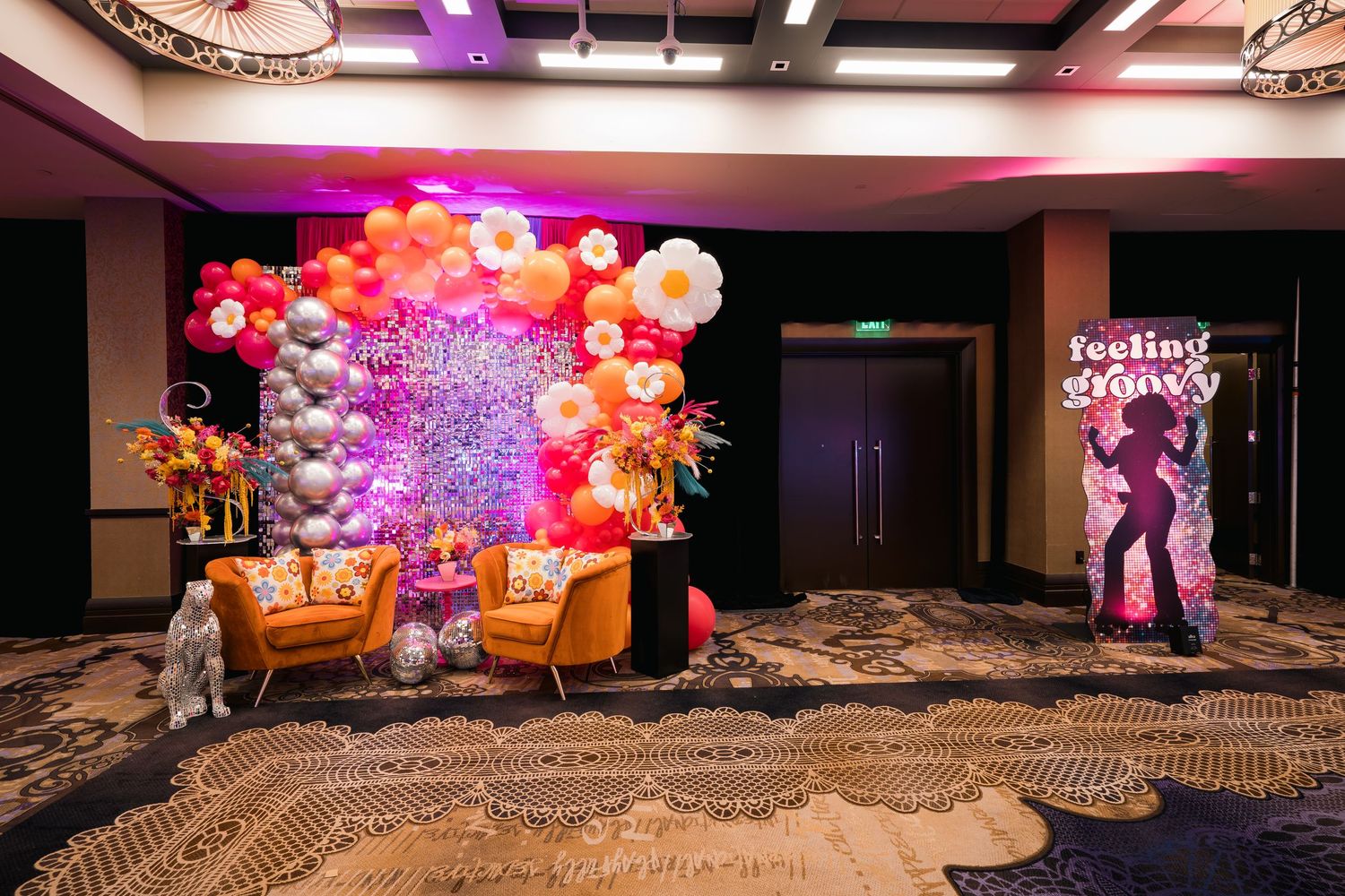 Luxurious photo backdrop with balloon garland and orange velvet seating area.