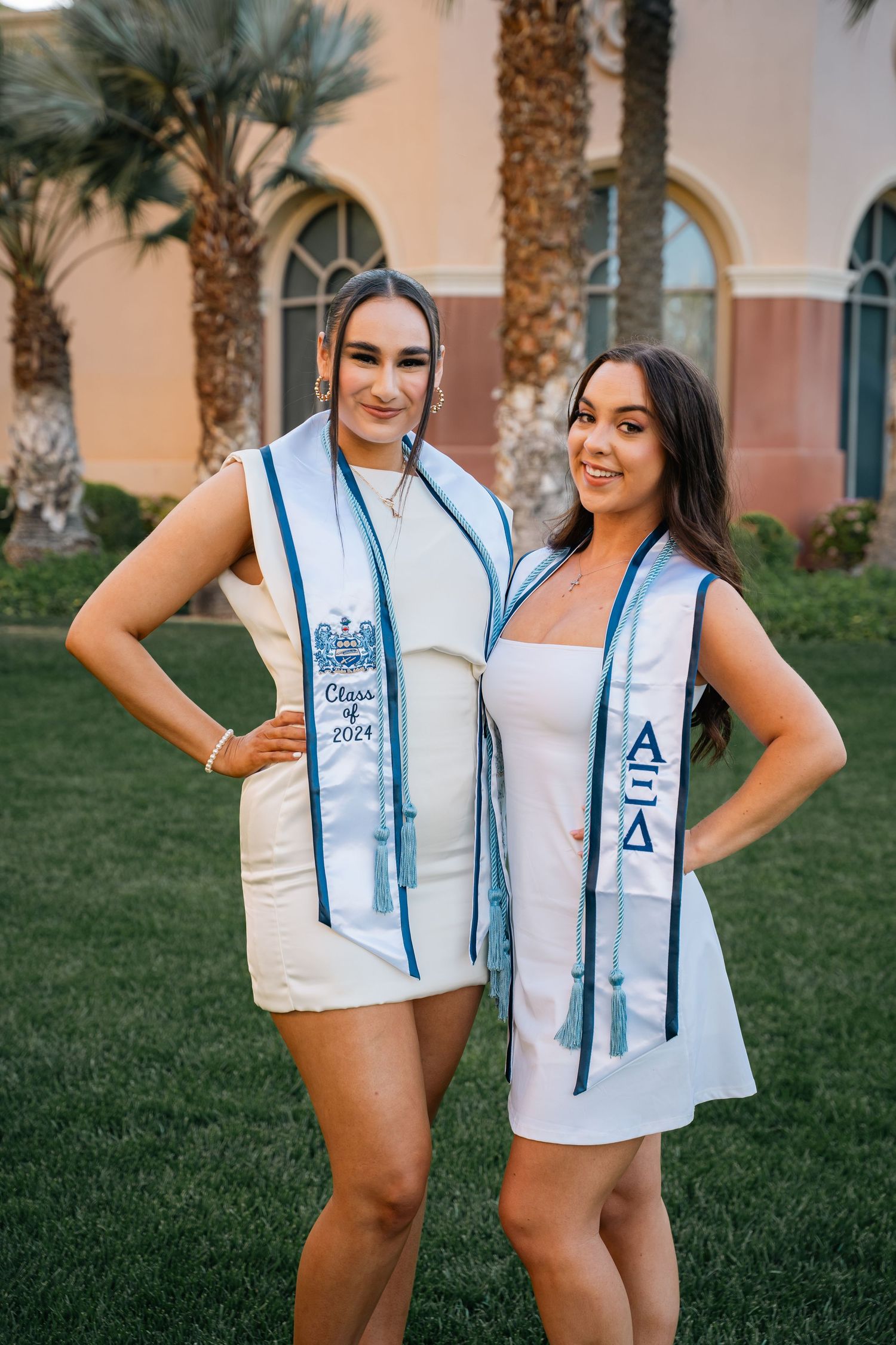 Two sorority members in white dresses display their matching light blue AΞΔ stoles.
