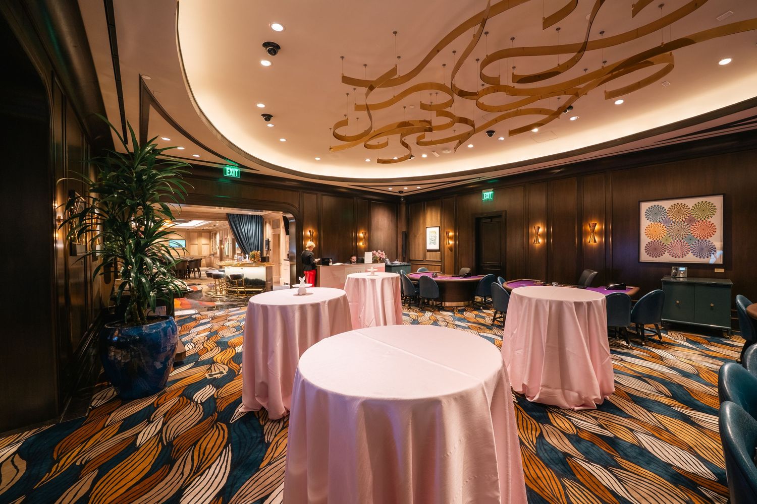 Upscale event space with pink tablecloths and artistic ceiling designs in warm ambient lighting.