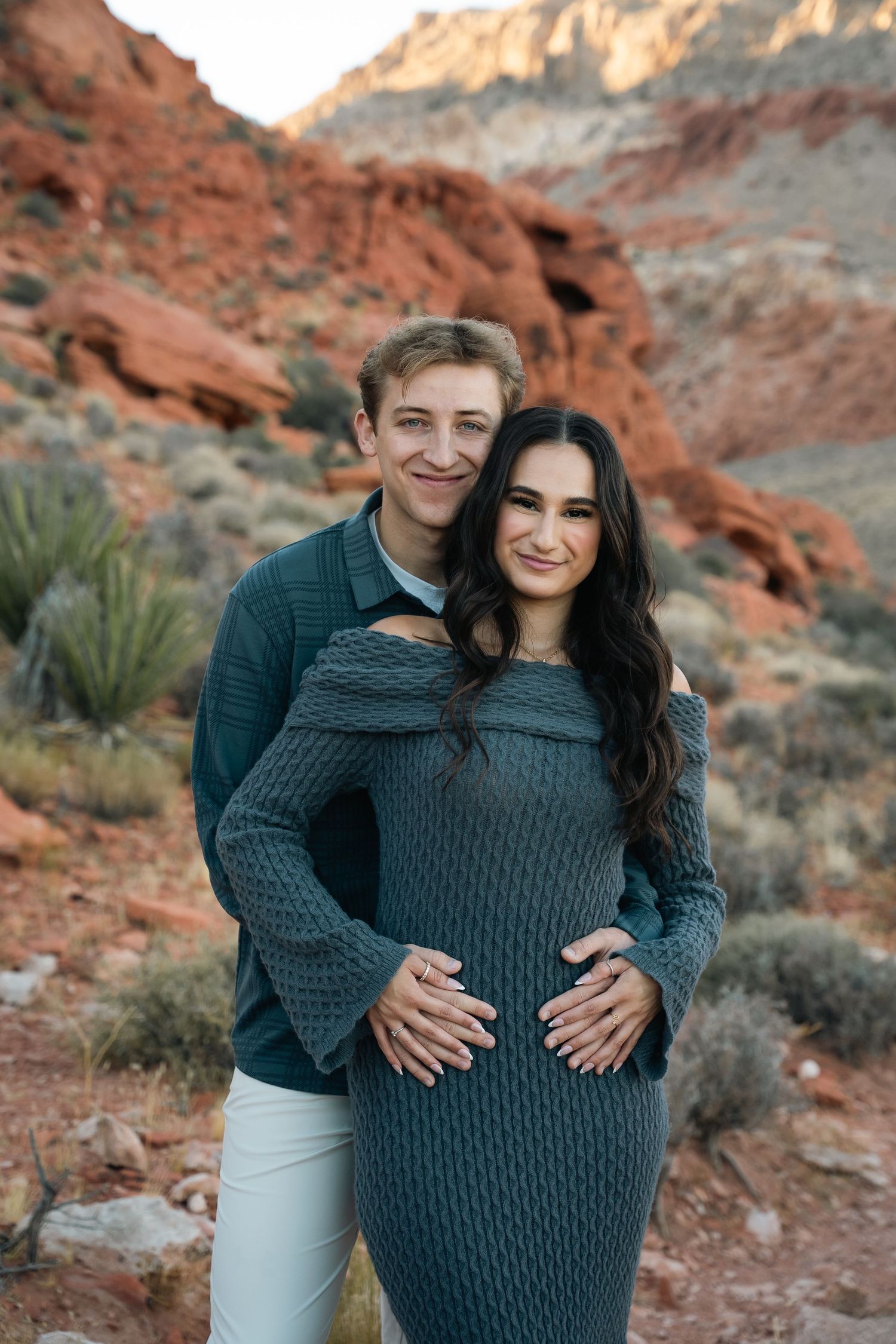 Couple in coordinated outfits embrace in front of desert landscape.