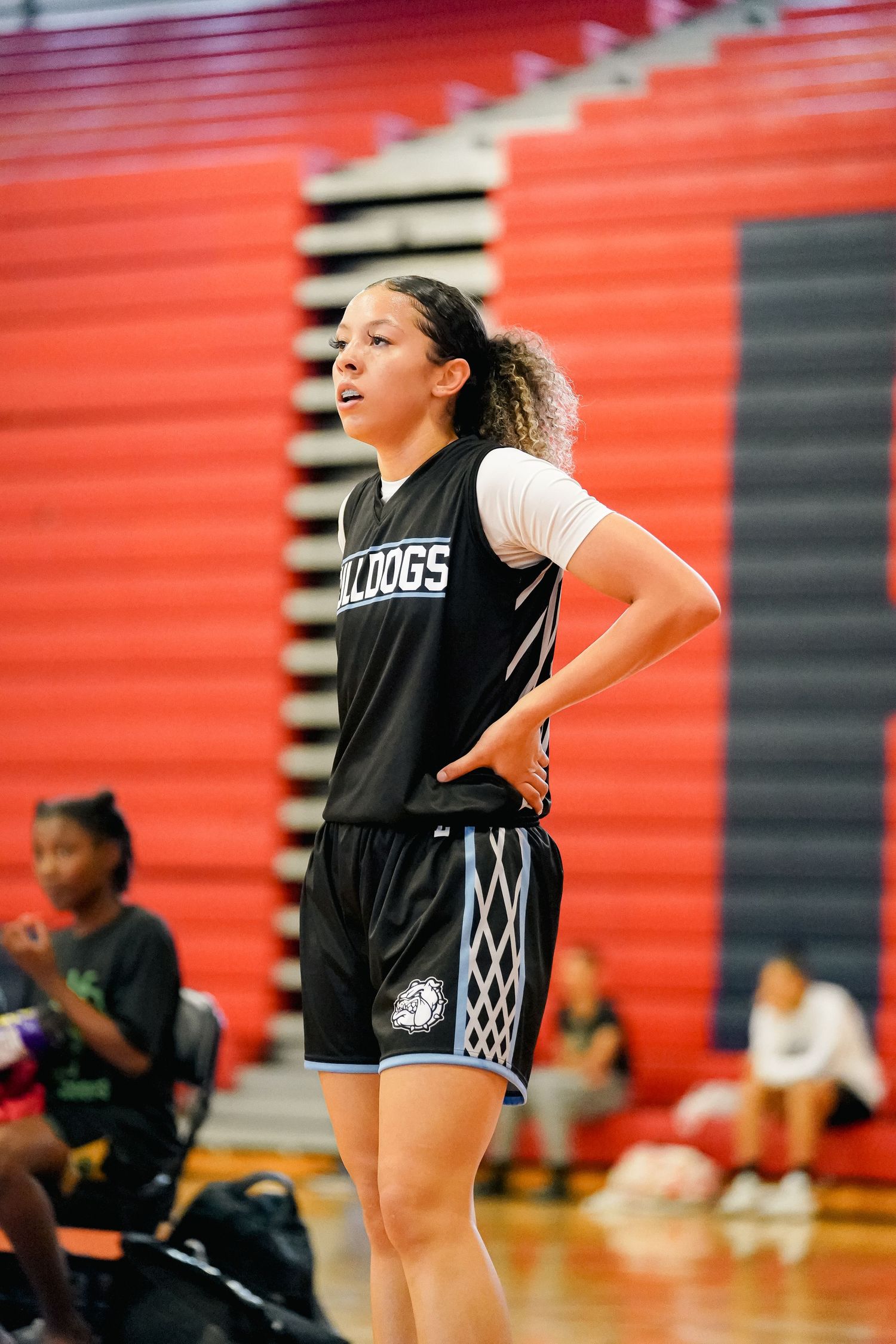 Basketball player in Kings uniform stands on sideline during game with red wall background.