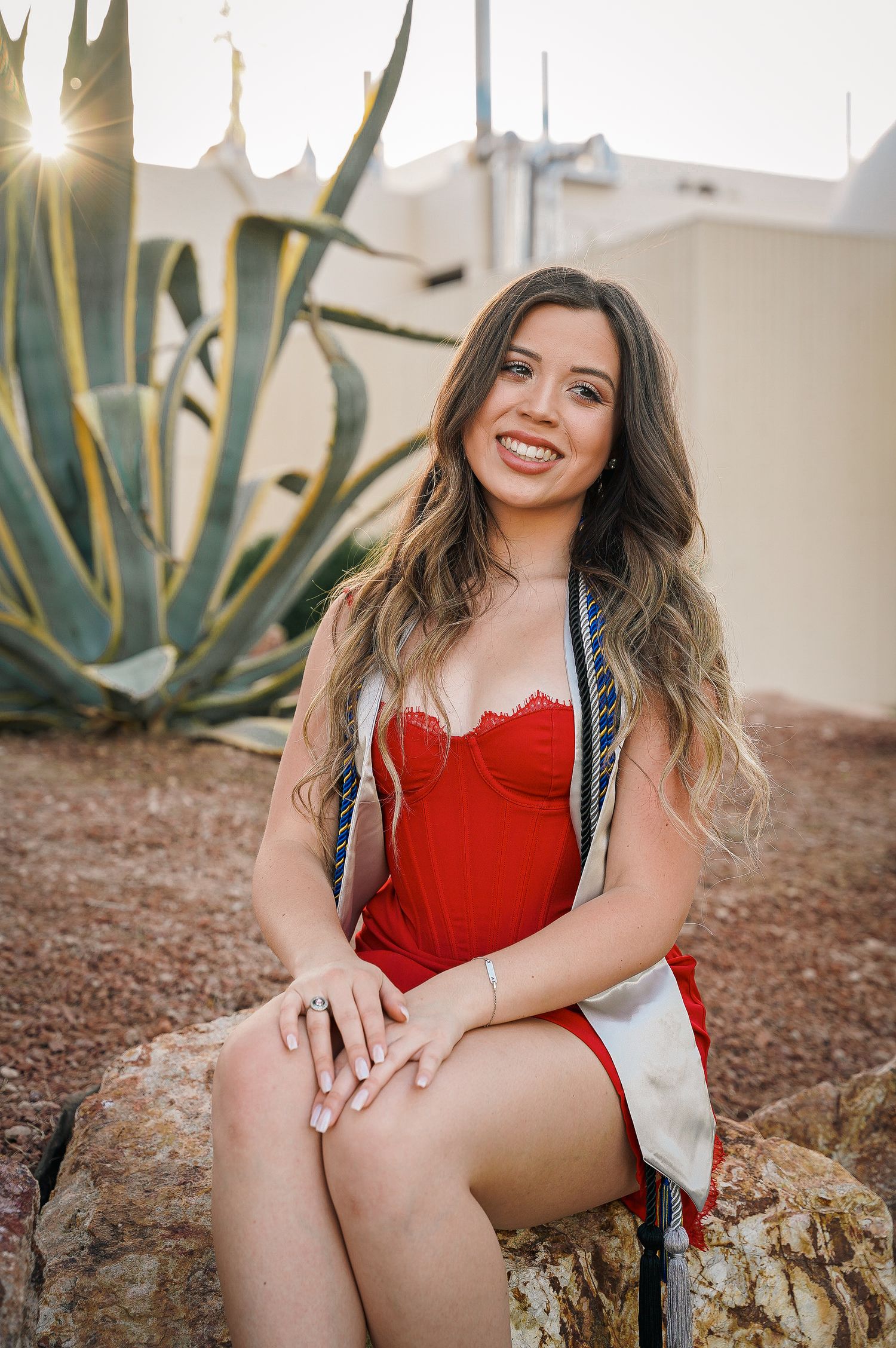 Portrait in red dress with graduation stole against desert landscape with agave plant.
