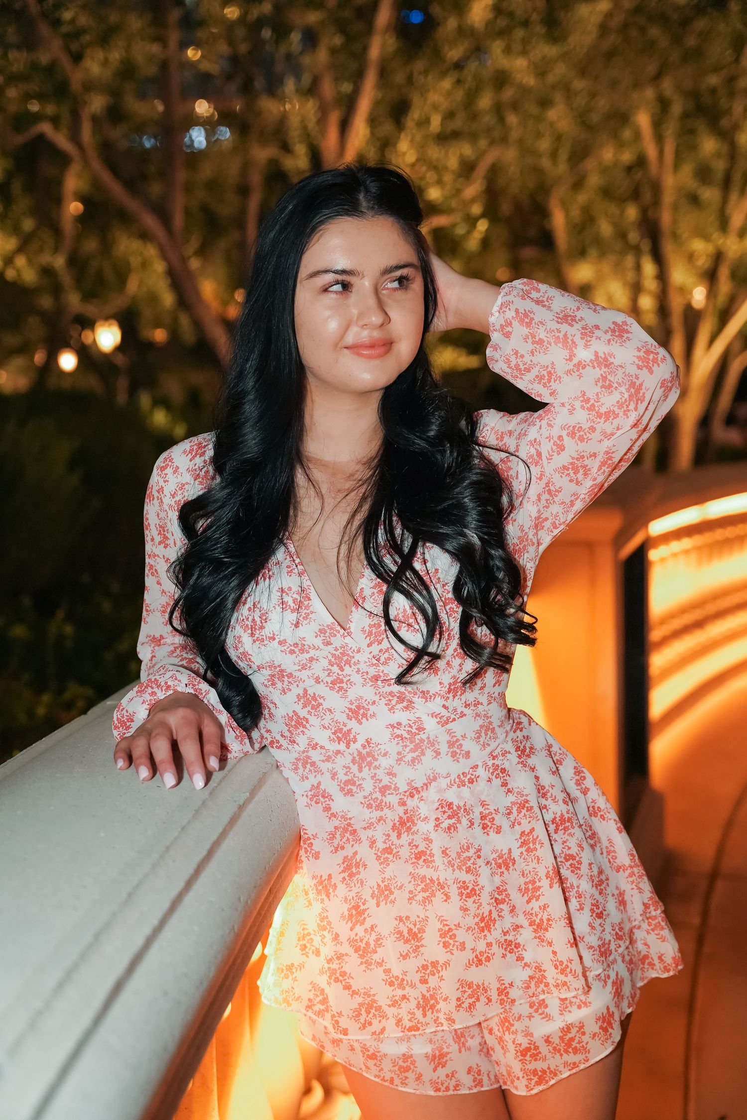 Woman in floral wrap dress poses outdoors with warm evening lighting.