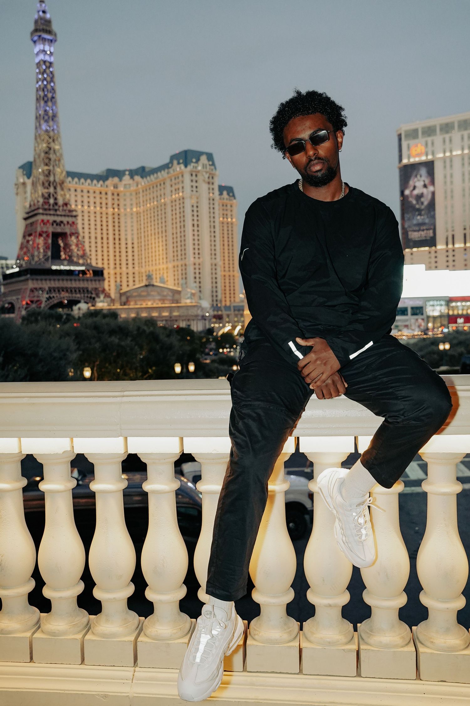 Person in black outfit sitting on balustrade with Paris Las Vegas hotel visible in background.
