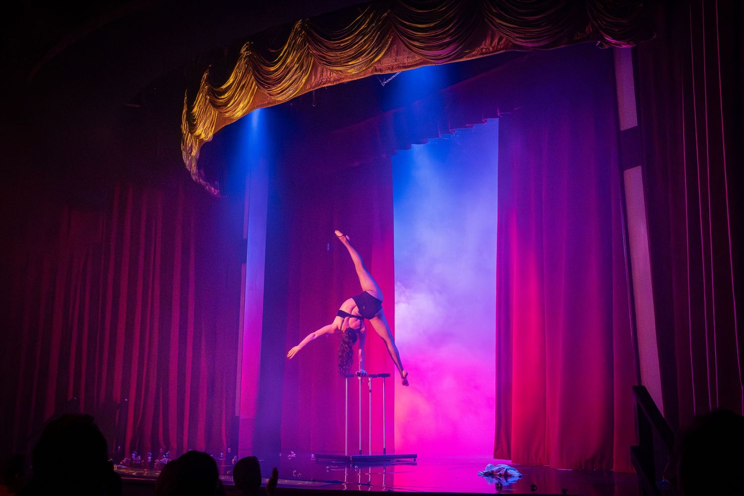 Aerial performer illuminated by dramatic purple and blue lighting on stage during a theatrical performance.
