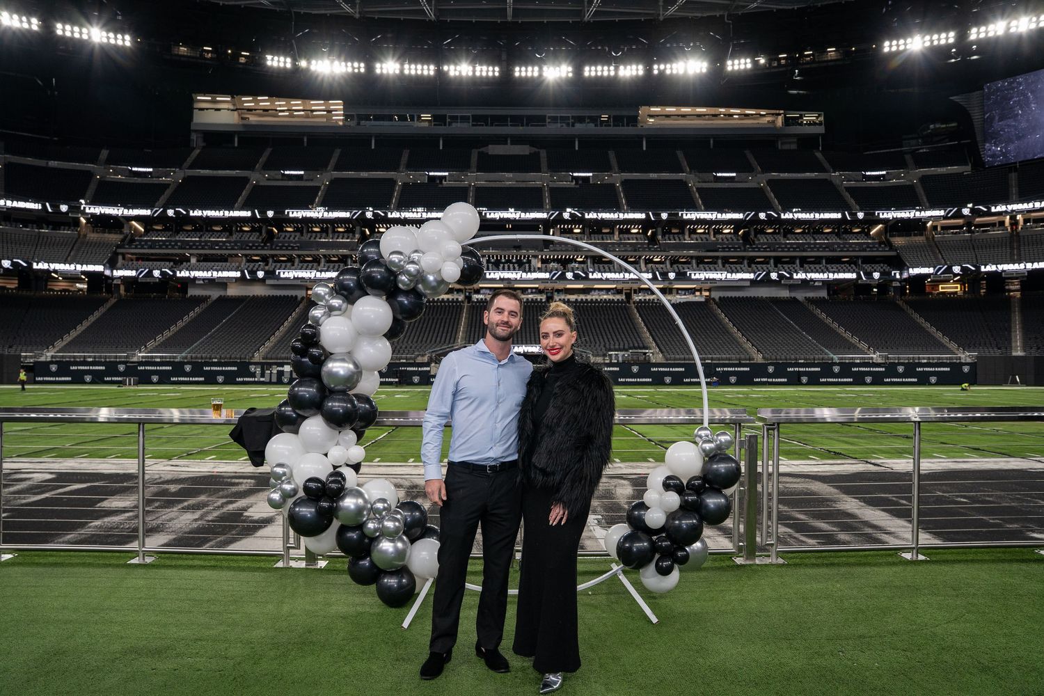 Two people stand together on a football field with decorative balloon display at indoor stadium.