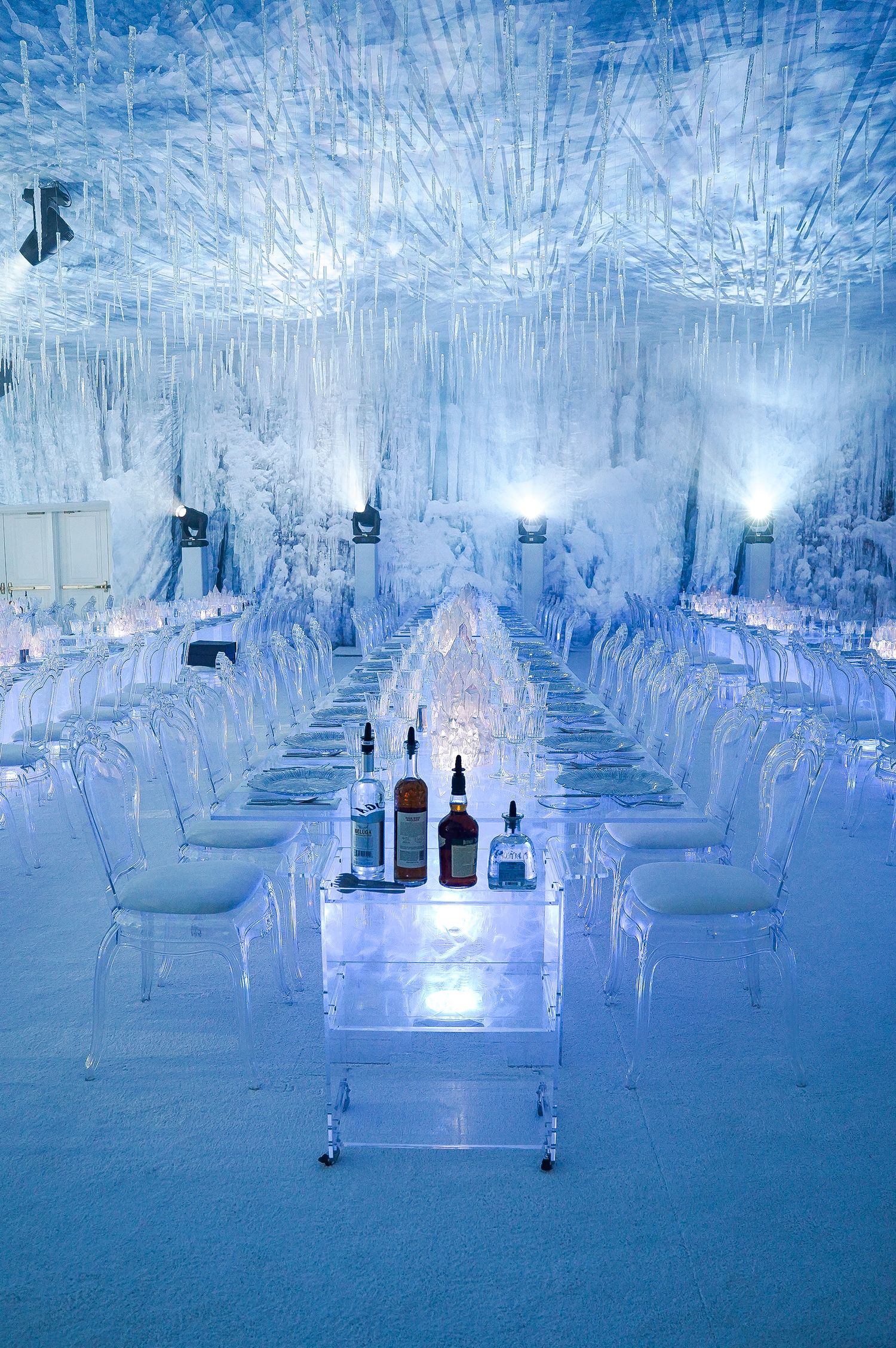 Ice-themed reception hall with clear chairs and bottles displayed on transparent table.