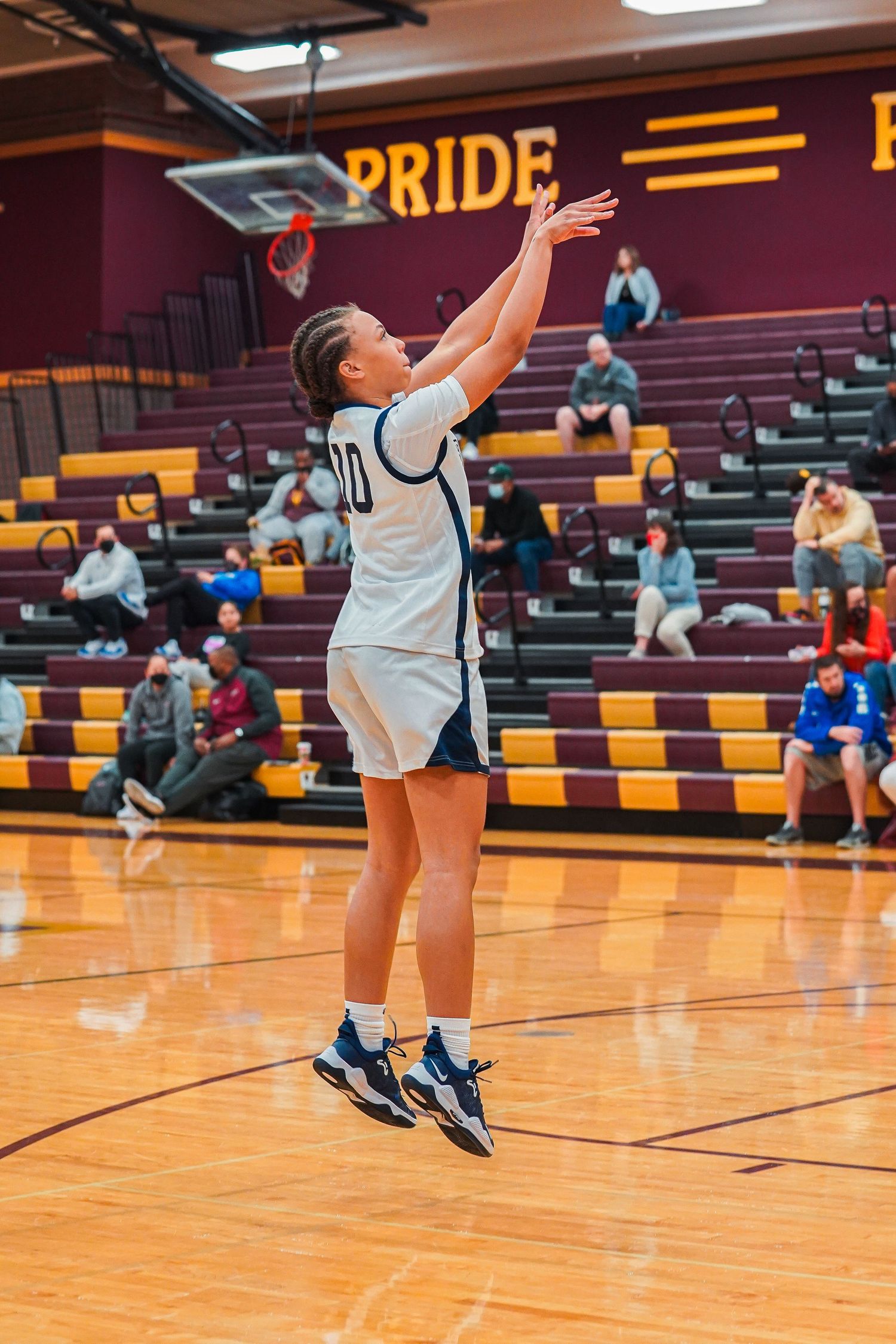 Player in white uniform shoots jump shot under Pride banner in gymnasium.