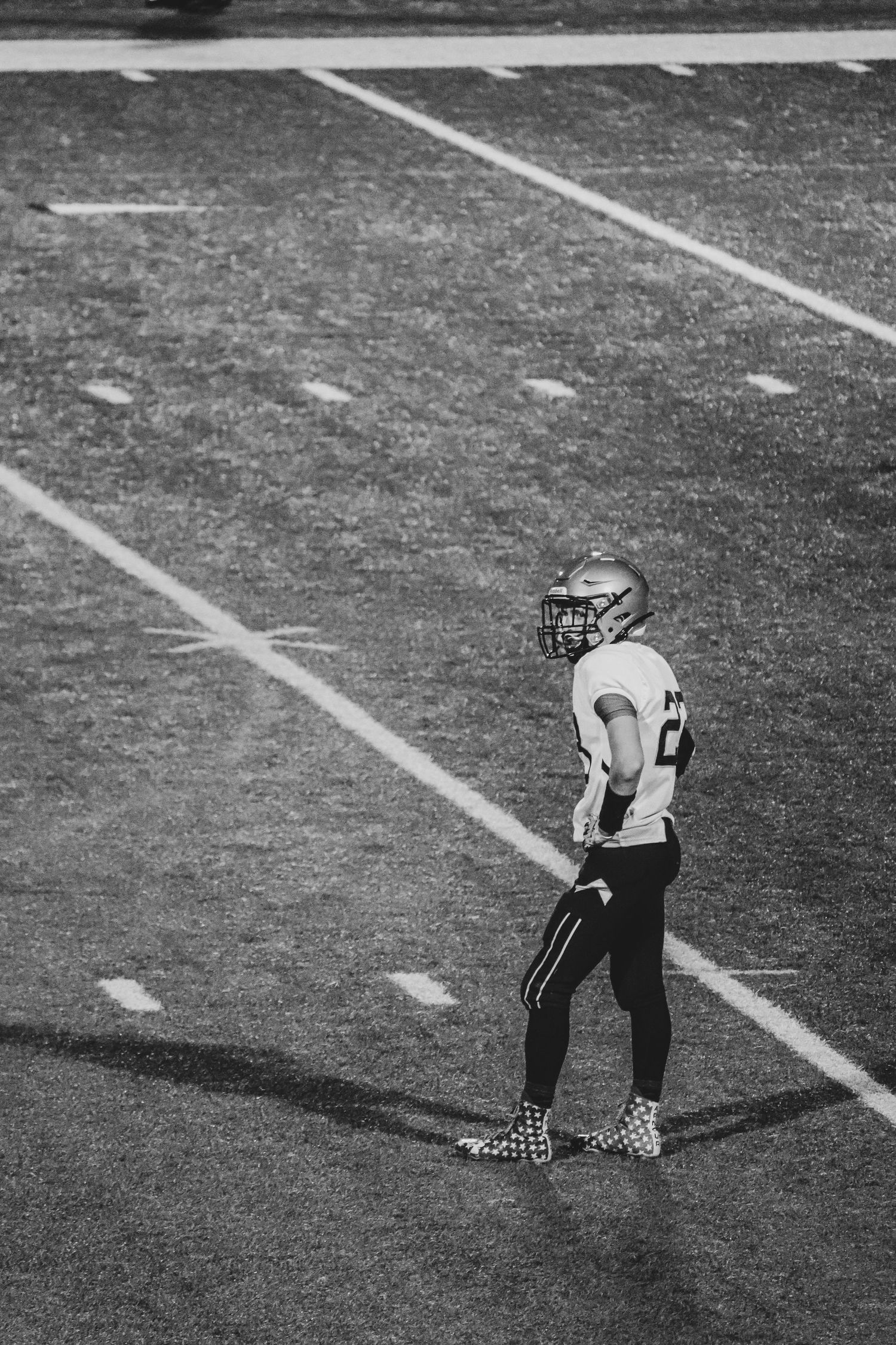 Football player in uniform standing alone on field during black and white game action shot.