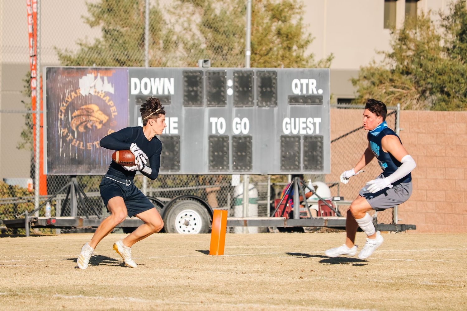 Athletes compete in flag football game with scoreboard visible in background.