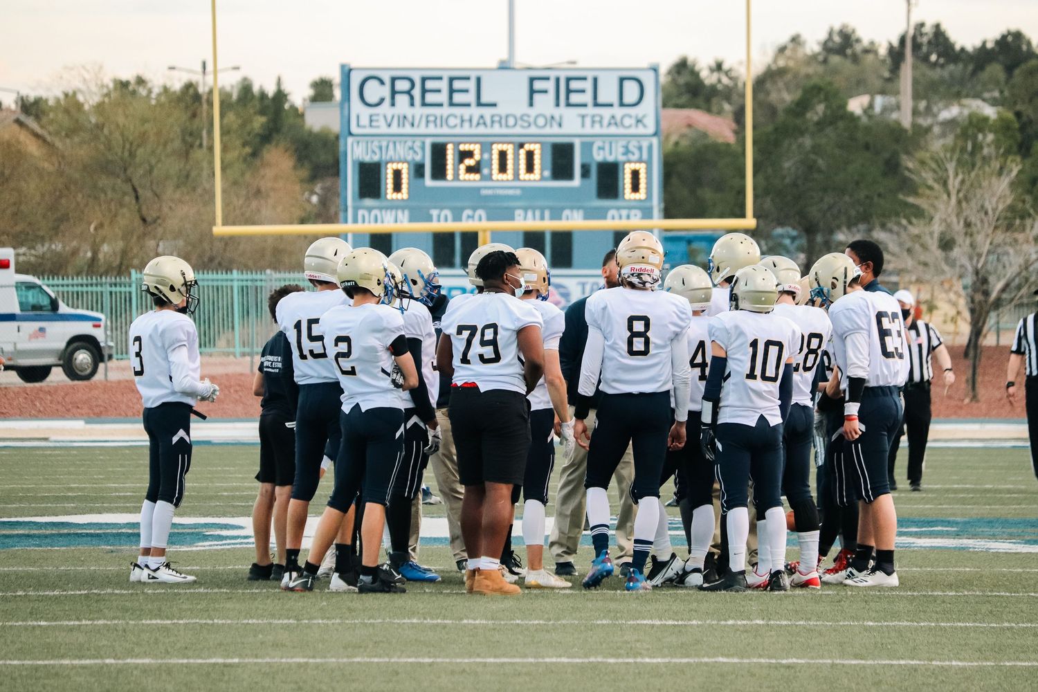 Football team huddles on Creel Field during practice or game.