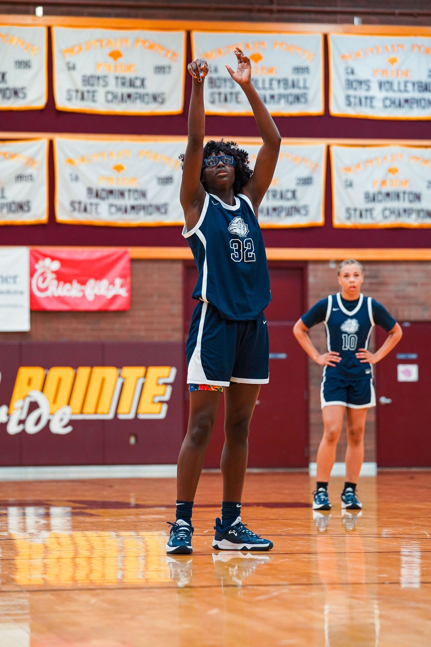 Basketball players in navy uniforms stand on a glossy wooden court with championship banners displayed on the wall.