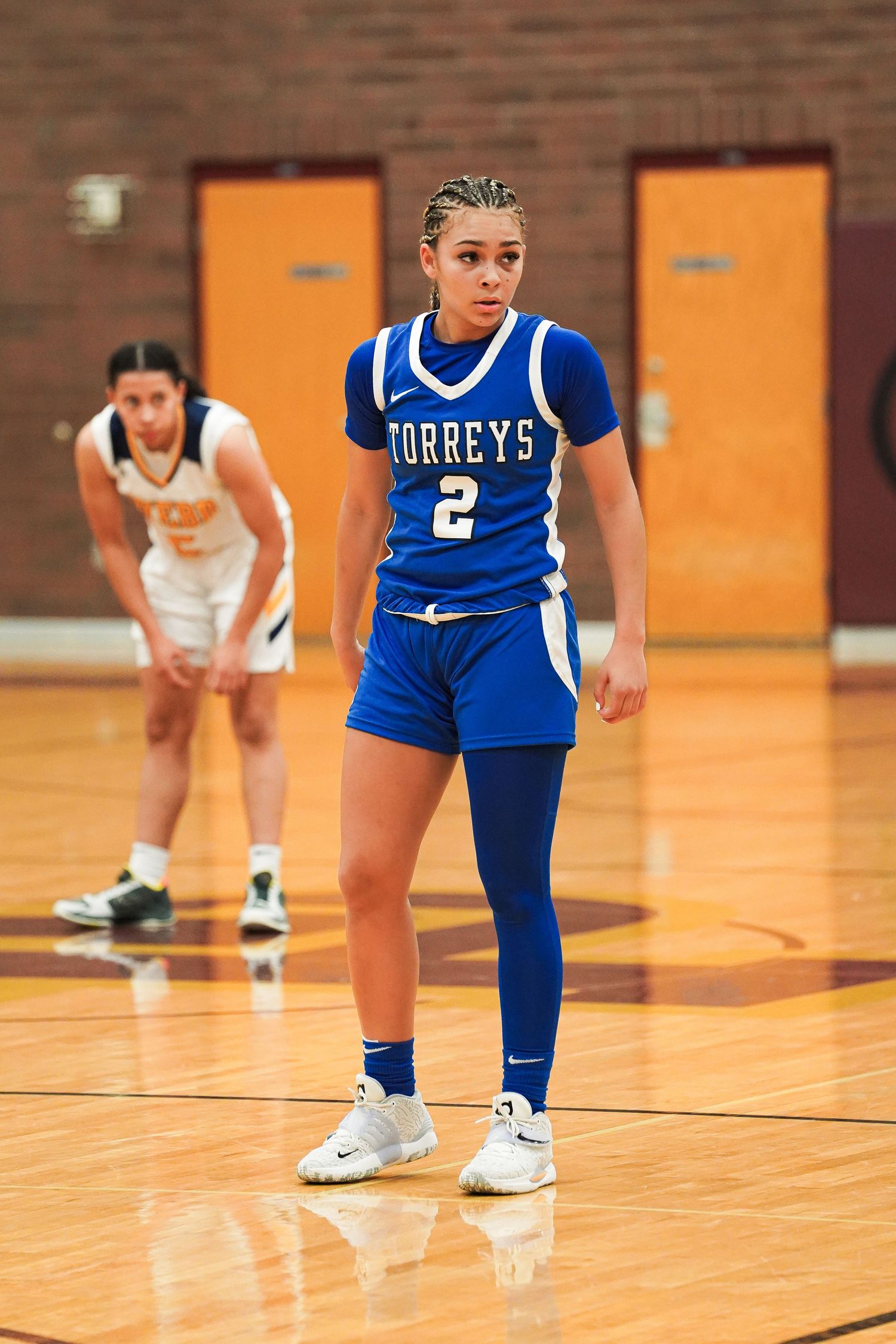 Basketball player in blue Torreys uniform standing ready on wooden court.