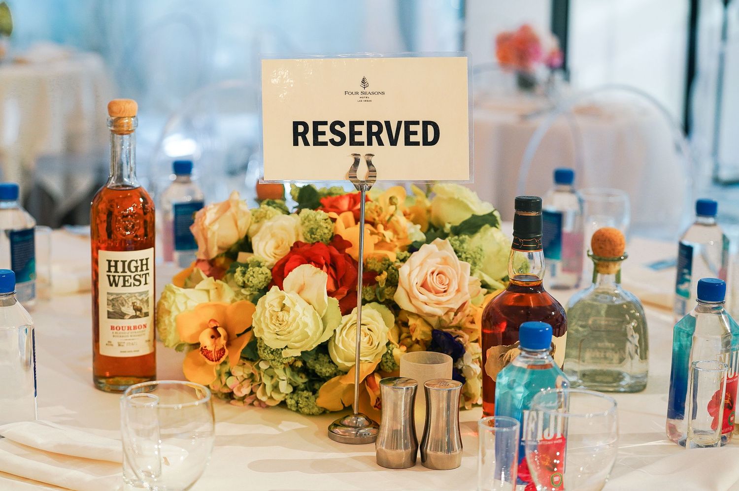 Reserved table setting with floral centerpiece and alcohol bottles at upscale event.