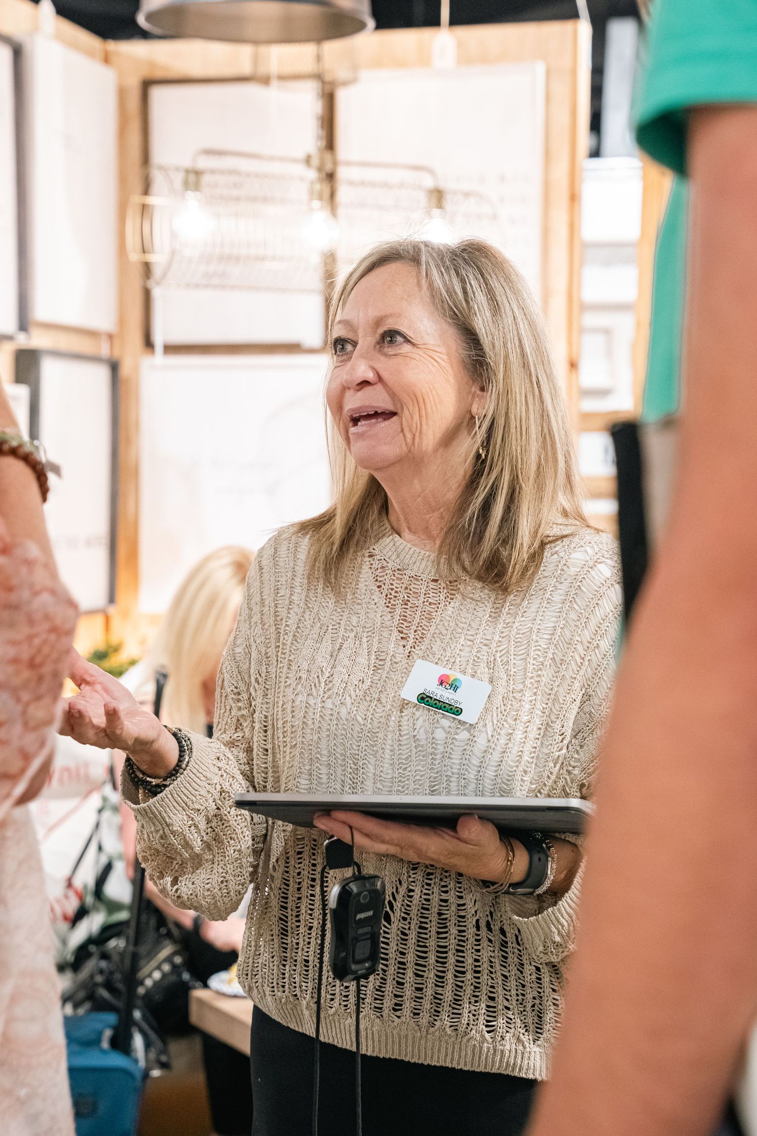 A person holding a tablet smiles while assisting customers in a retail setting with wooden displays.