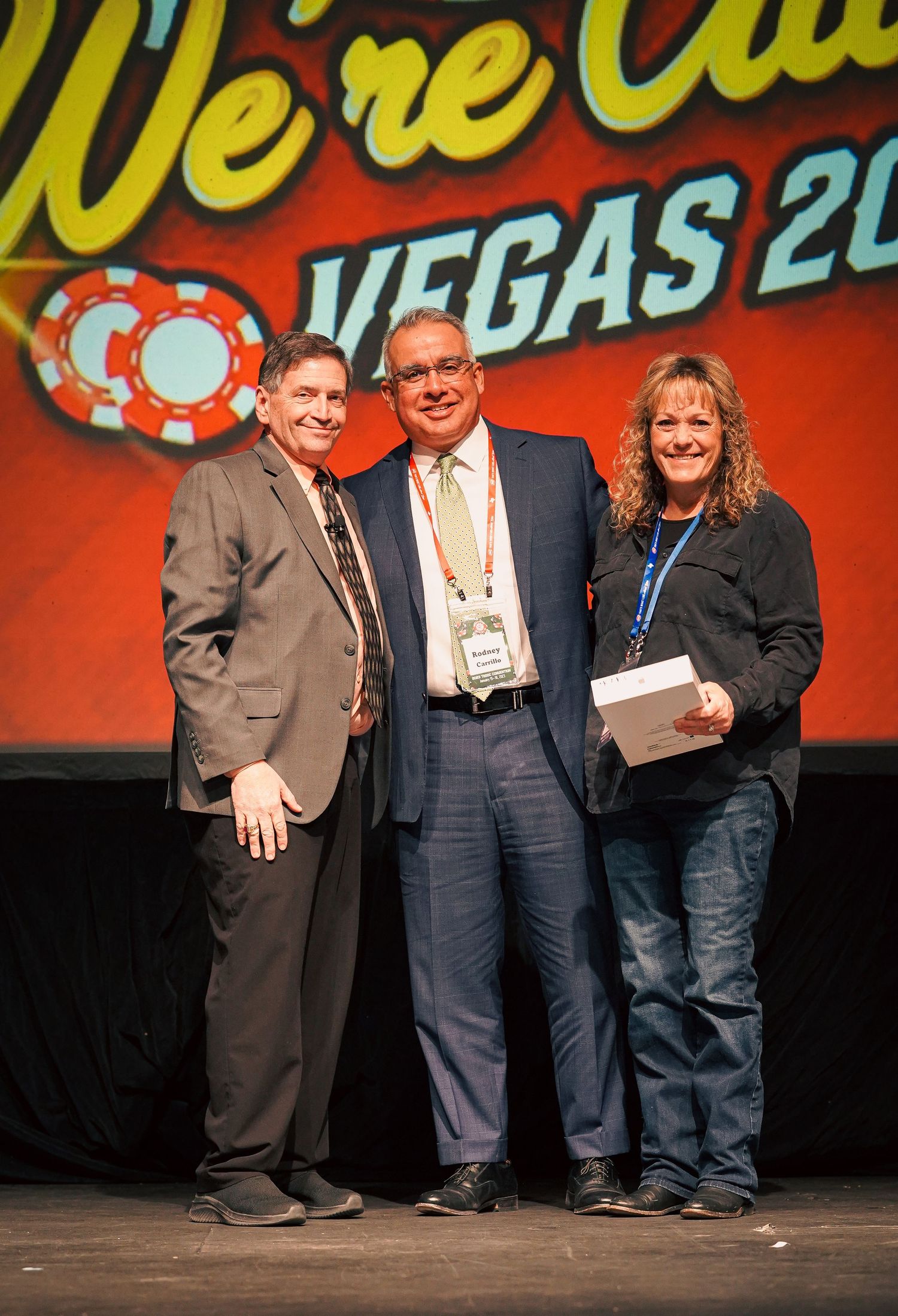 Three people pose for group photo at Vegas conference with illuminated backdrop.