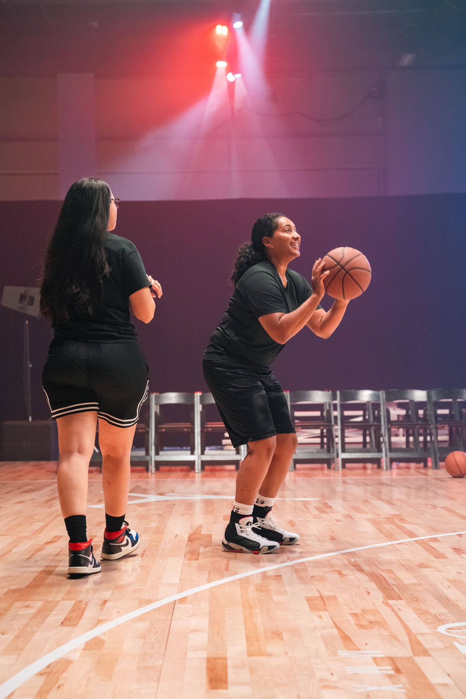 Basketball player practicing shooting form on indoor court under dramatic red lighting.