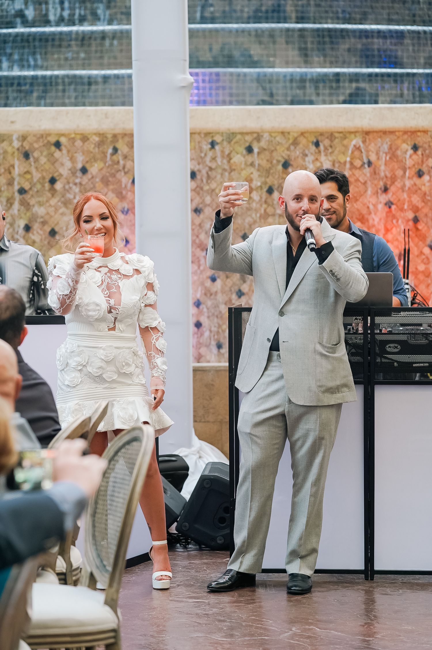 Two people making toasts at celebration with decorative wall backdrop.
