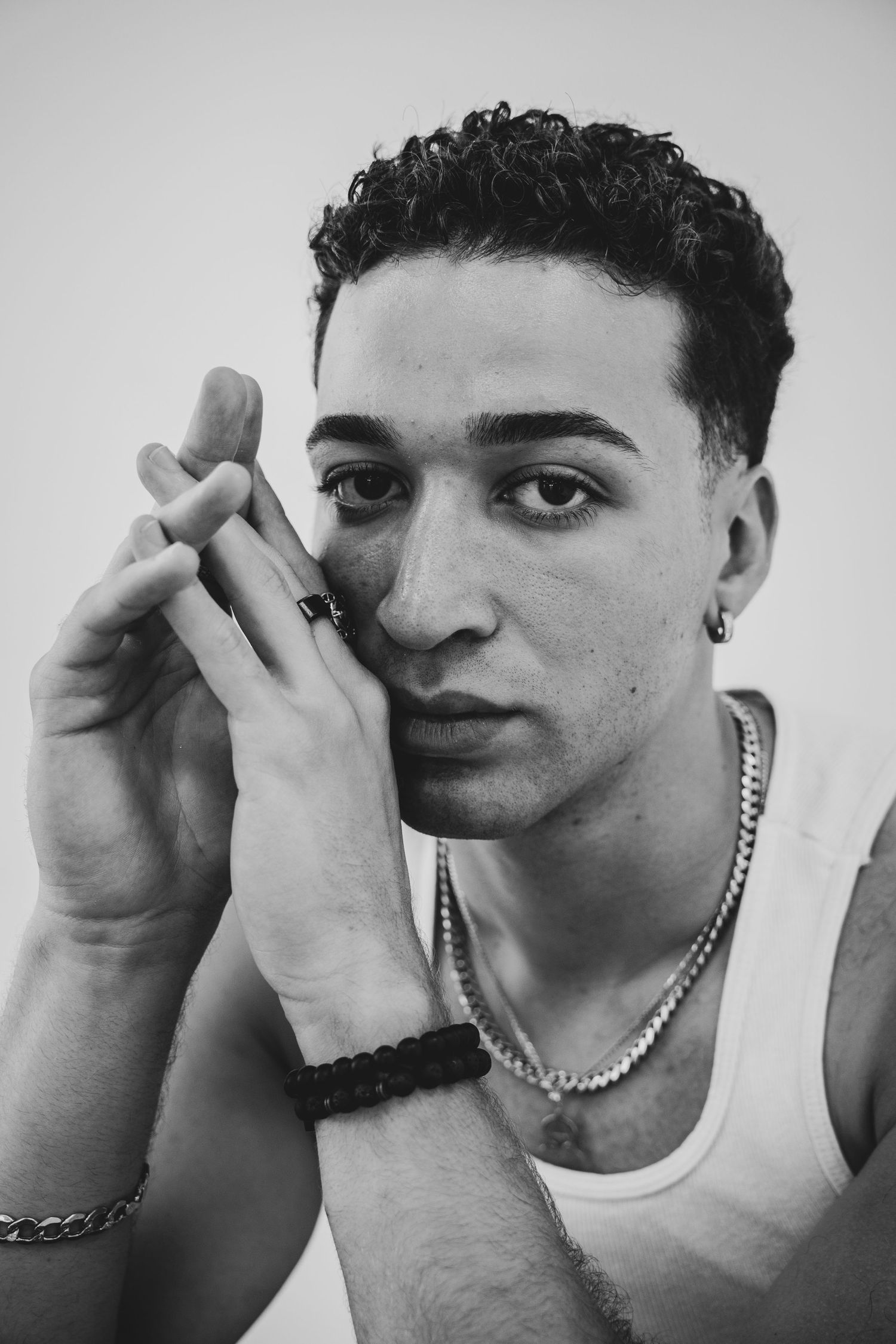 Artistic portrait showing a model with jewelry and tank top in dramatic black and white lighting.