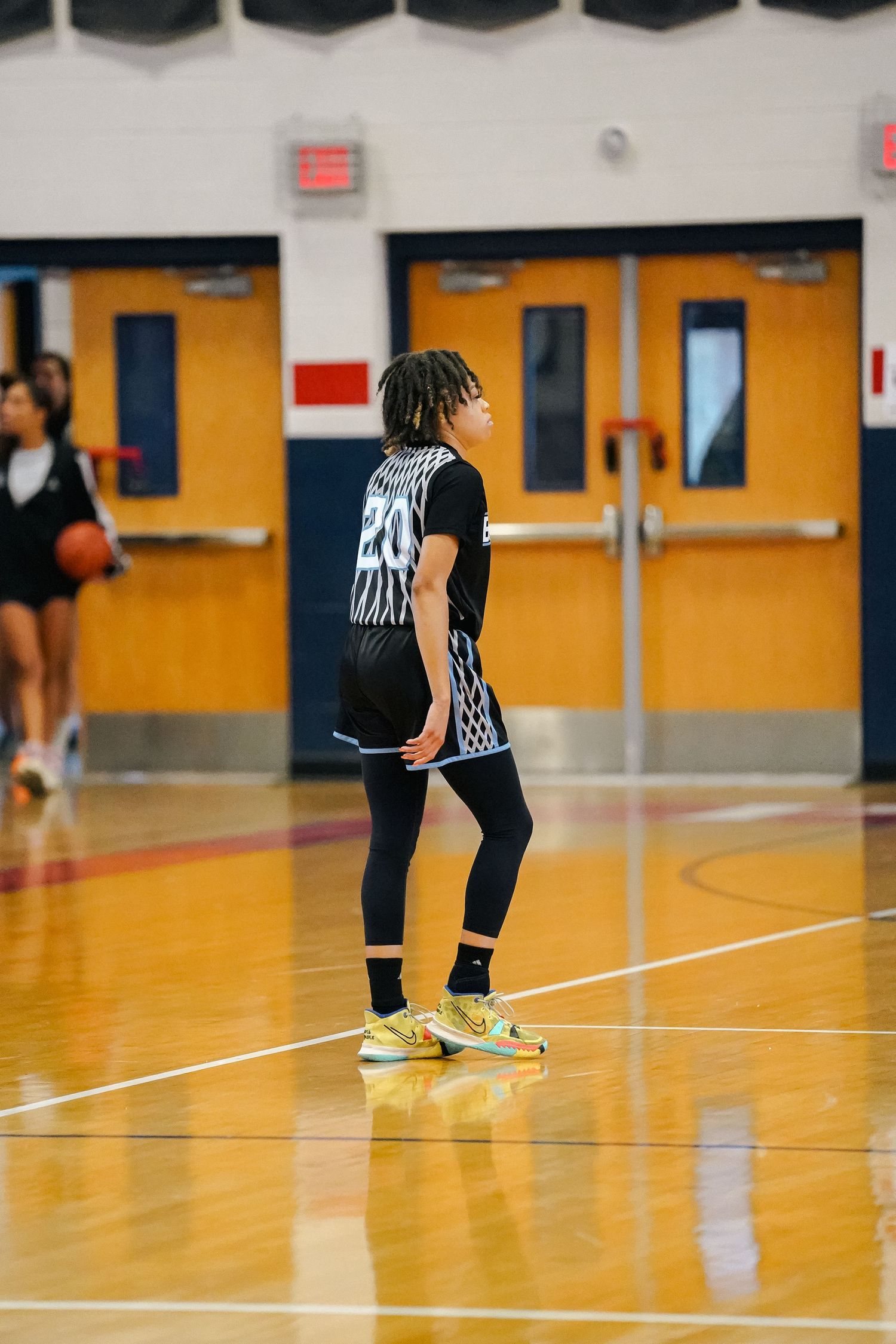 Basketball player in black and white uniform stands on court with yellow doors in background.