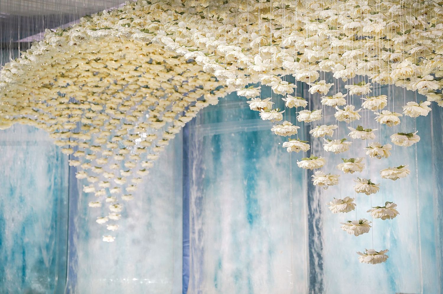 Stunning ceiling installation featuring hundreds of hanging gold paper flowers against a blue watercolor backdrop.