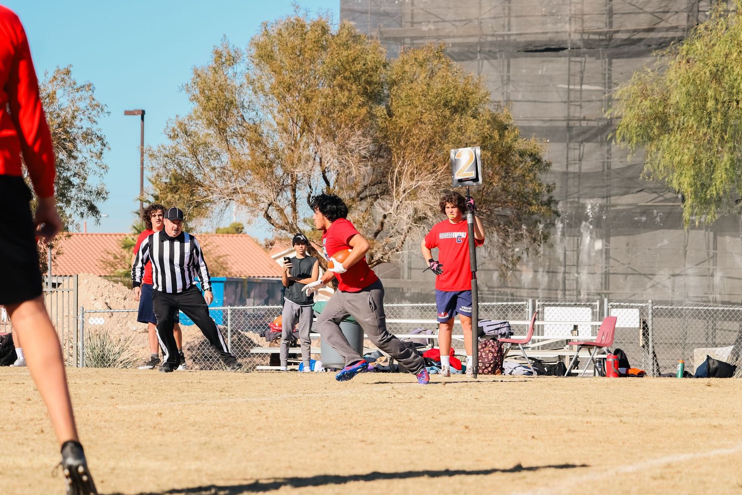 A flag football game in progress on a sunny field with officials and spectators watching.