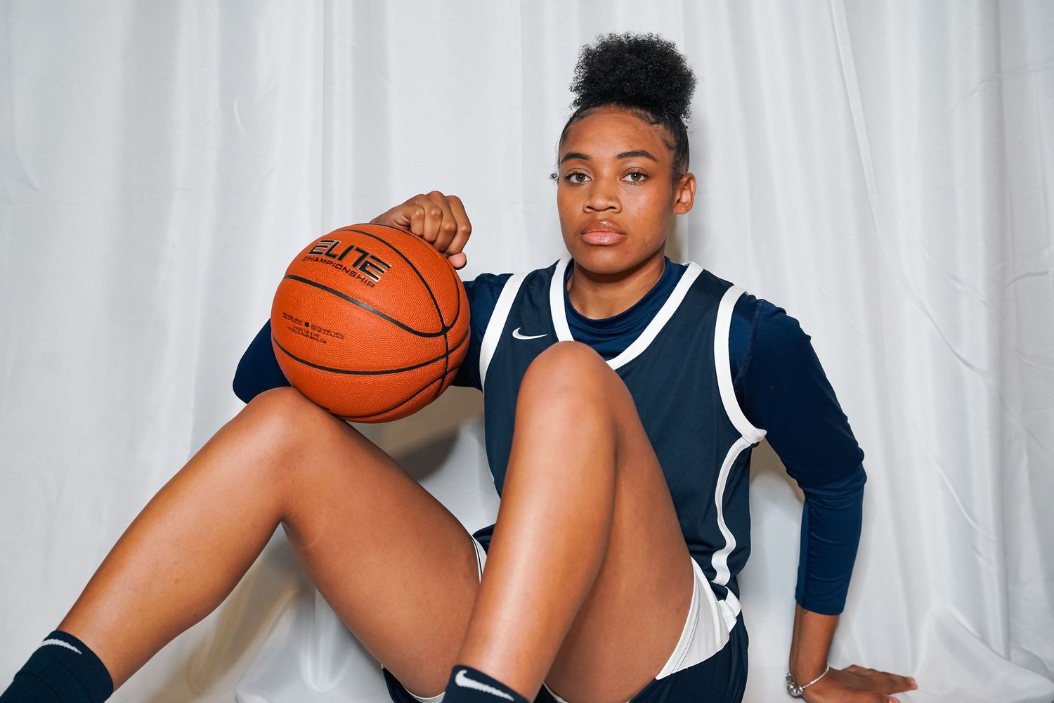 Basketball player in navy uniform poses with ball against white backdrop.