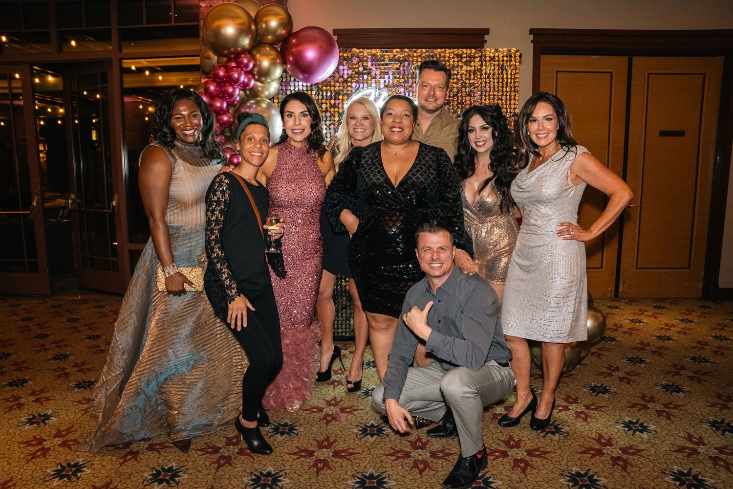 Group photo of party guests posing together in front of a balloon arch at an evening celebration.