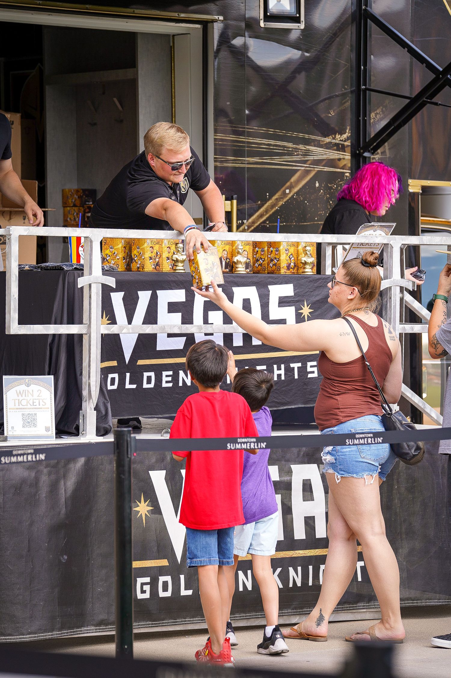 People interact with staff at Vegas Golden Knights merchandise booth during outdoor event.