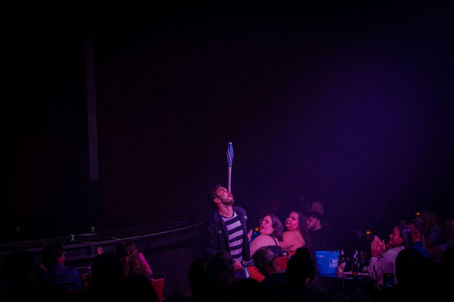 Theater audience silhouettes visible during purple-lit stage performance.