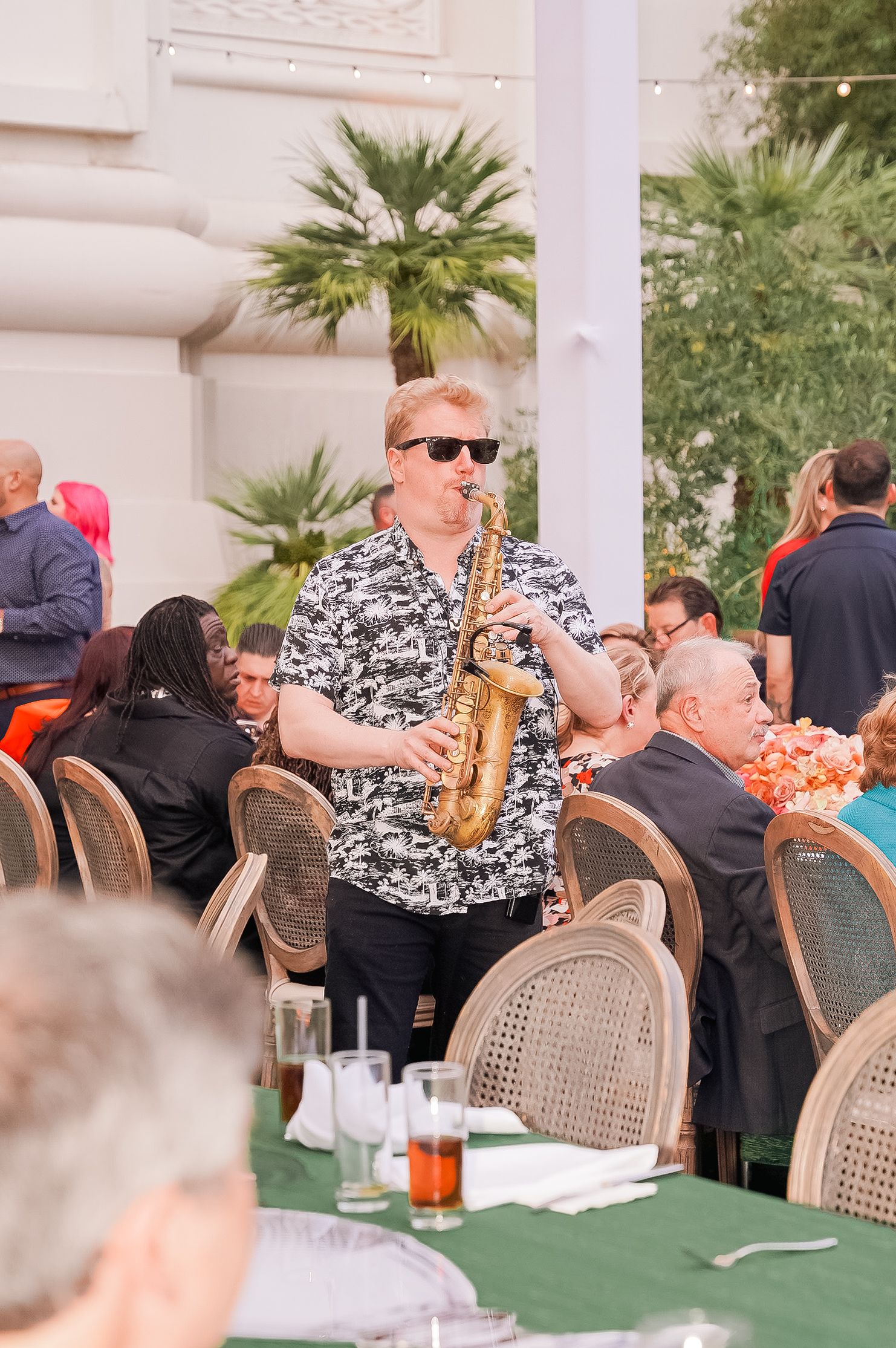 Musician in patterned shirt plays saxophone during outdoor dining event.