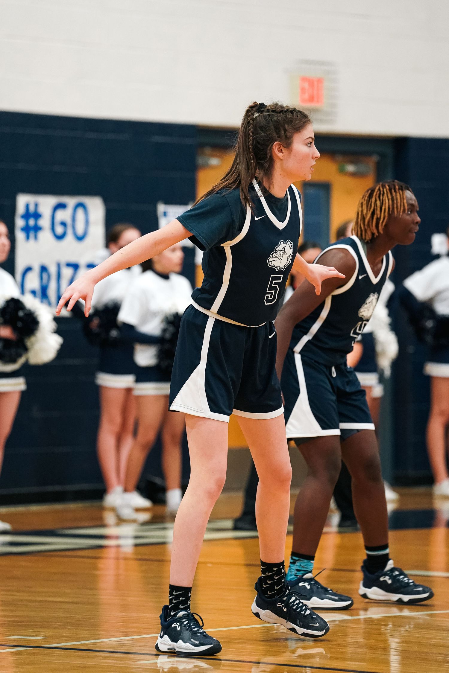 Basketball players in navy uniforms lined up in defensive stance on court.