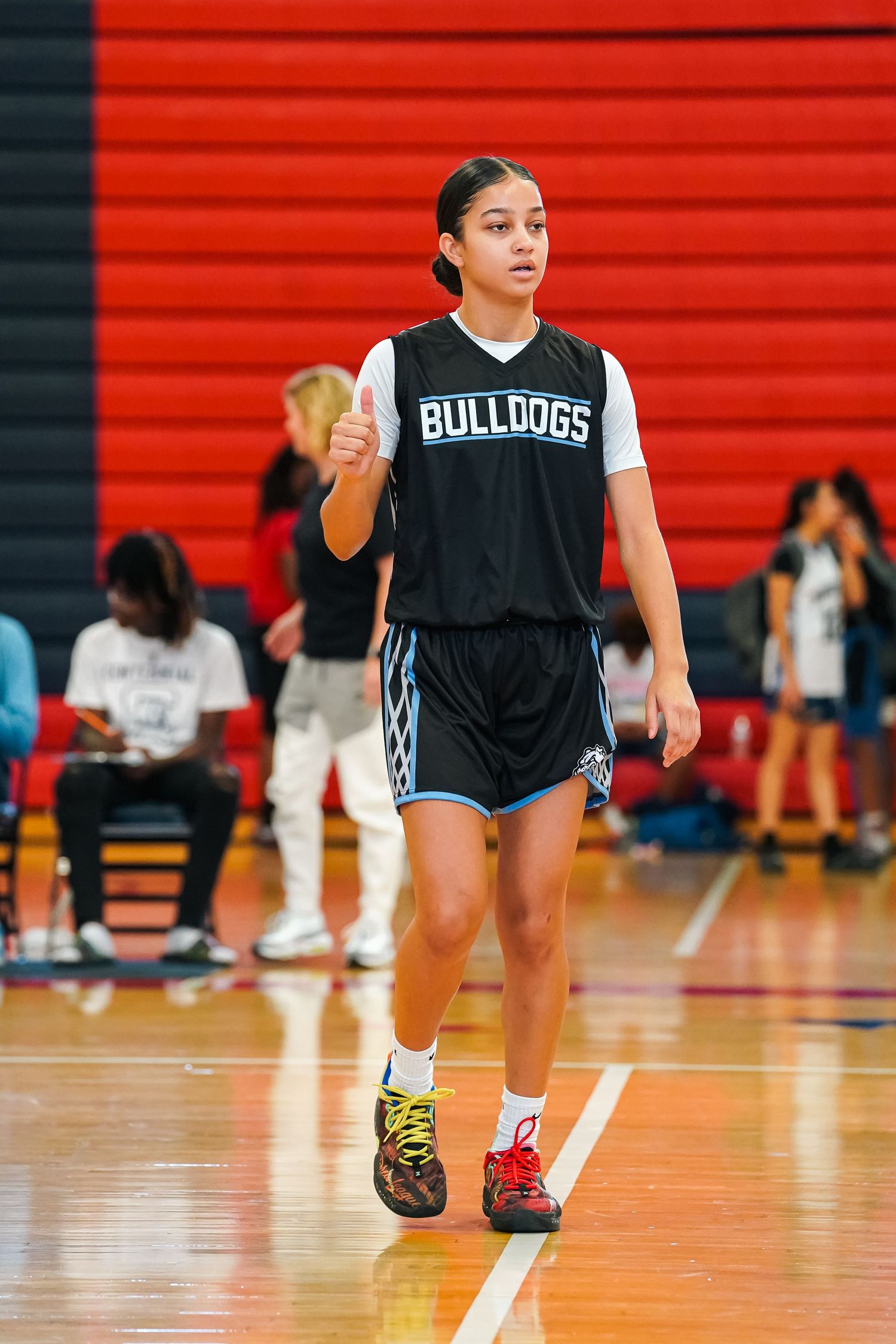 Basketball player in Bulldogs uniform performs stretching exercises on gymnasium floor.