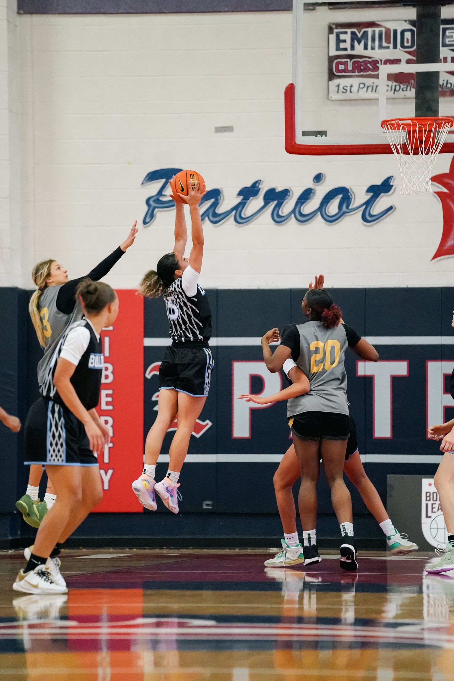 Players jump high to block shots during an intense basketball game in a school gymnasium.
