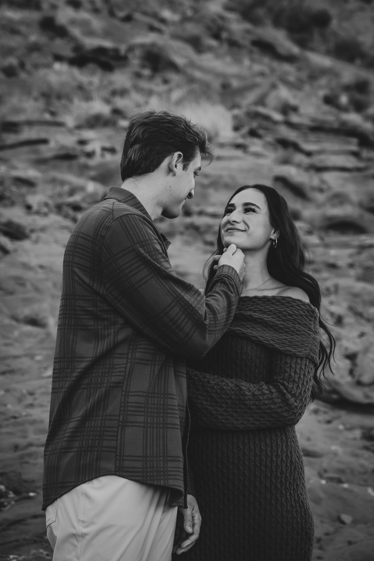A tender black and white moment between a couple in warm sweaters against desert cliffs.